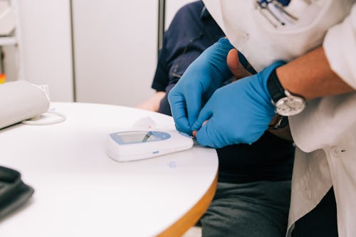 A healthcare professional wearing a handglove using a glucometer to test a patient's blood sample for blood glucose level