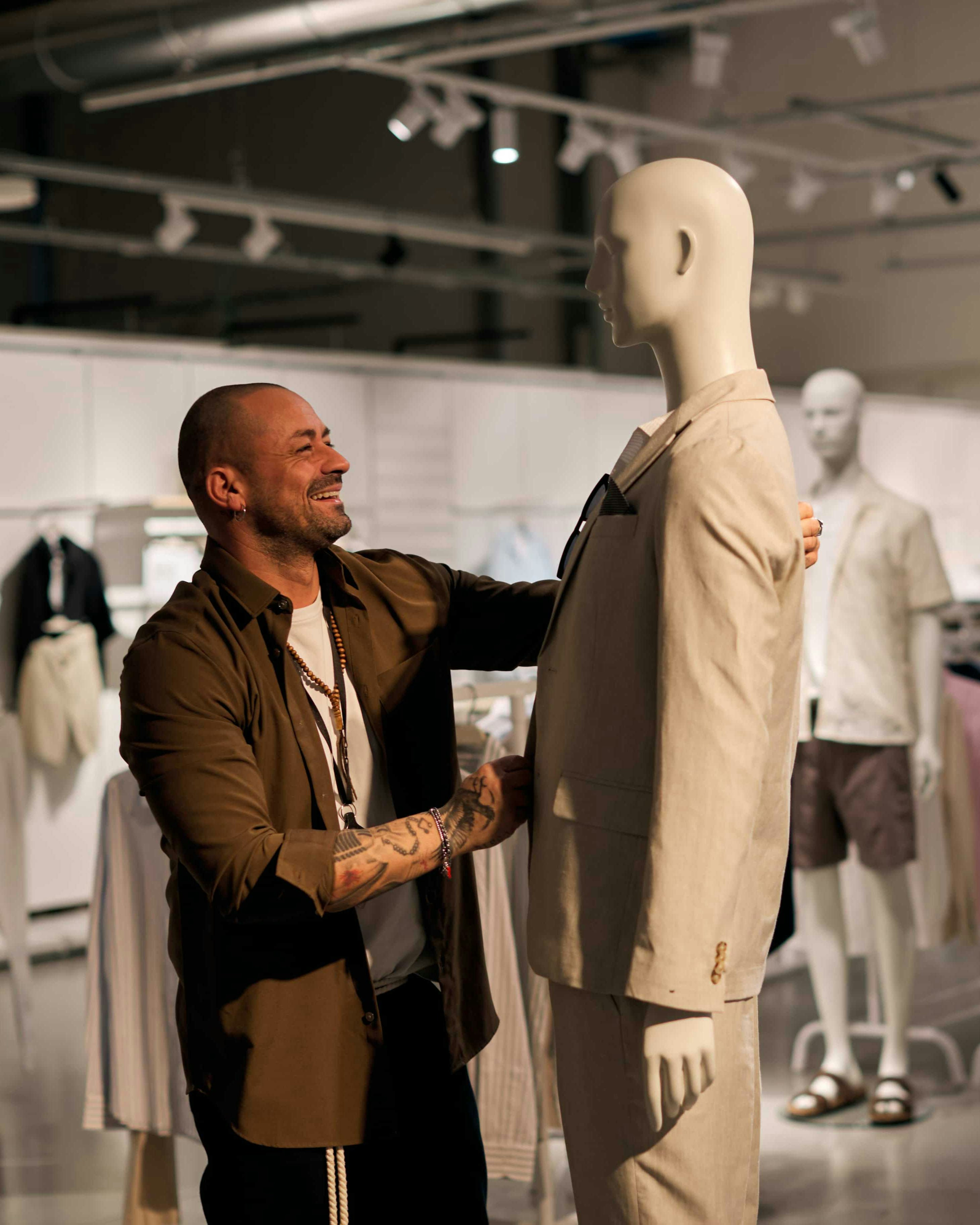 Uomo con blazer marrone che sistema un mannequin con giacca beige in uno showroom di moda