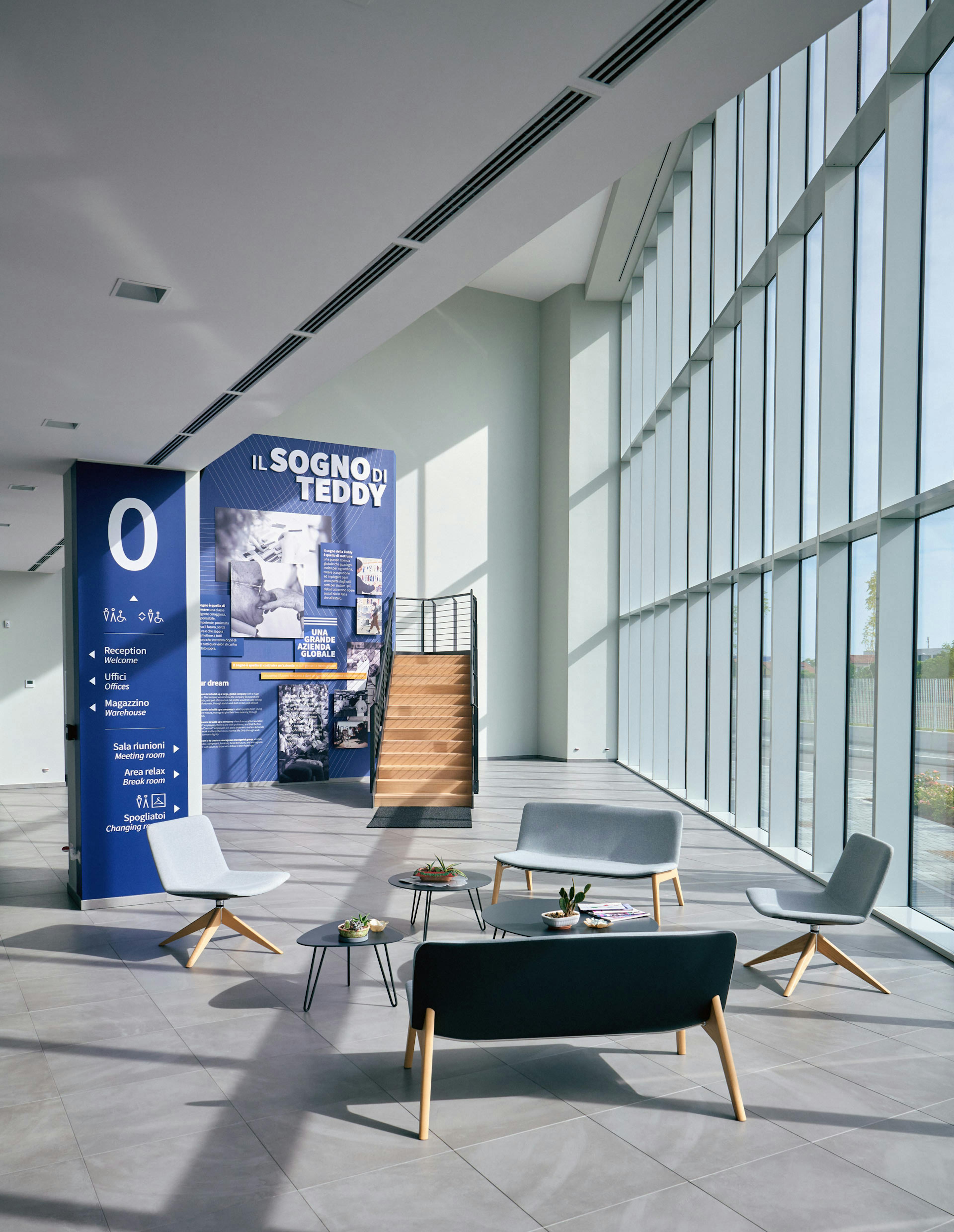 Area espositiva moderna con poltrone grigie e pannello informativo blu "Il Sogno di Teddy"