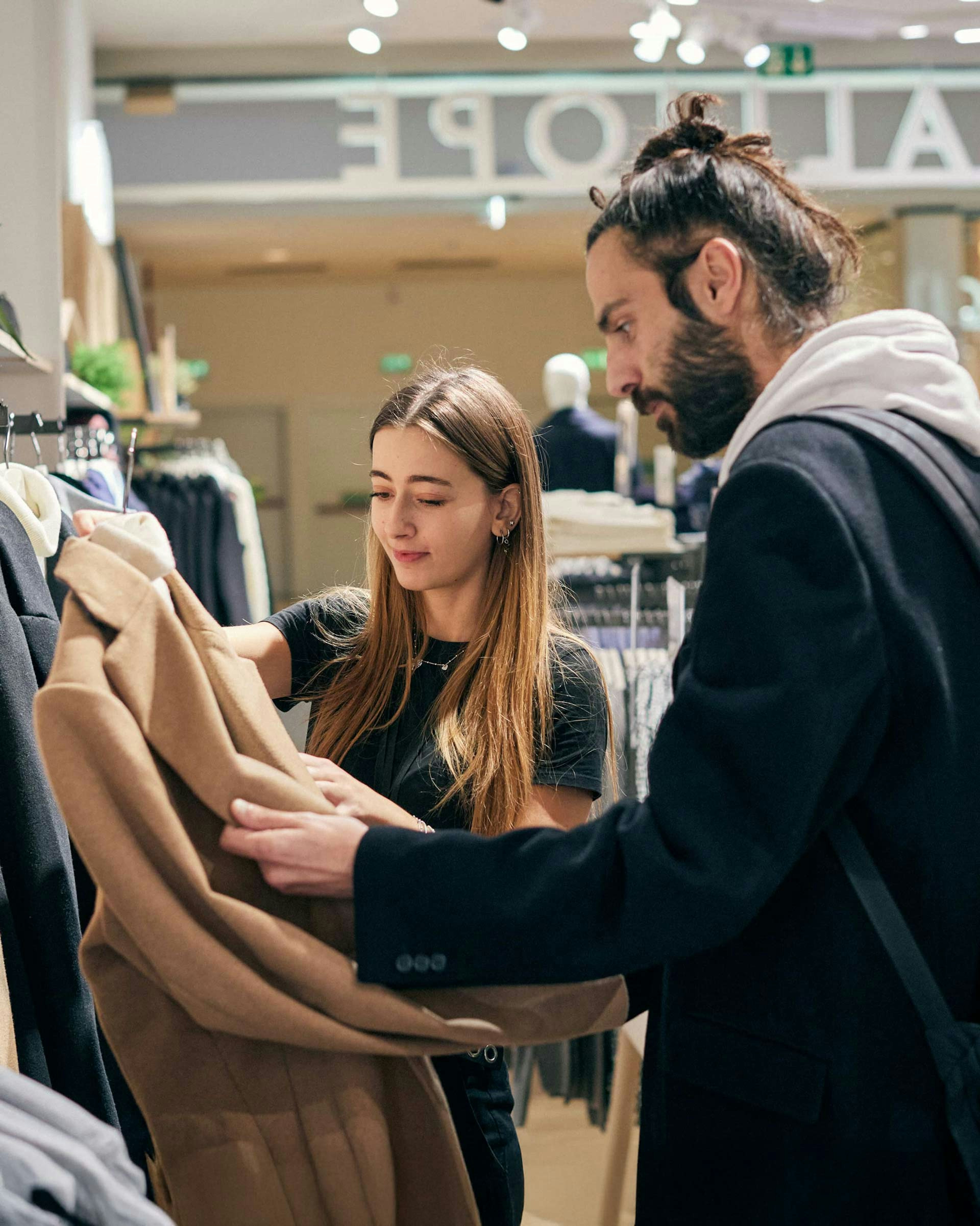 Uomo e donna esaminano insieme un cappotto beige appeso in un negozio di abbigliamento