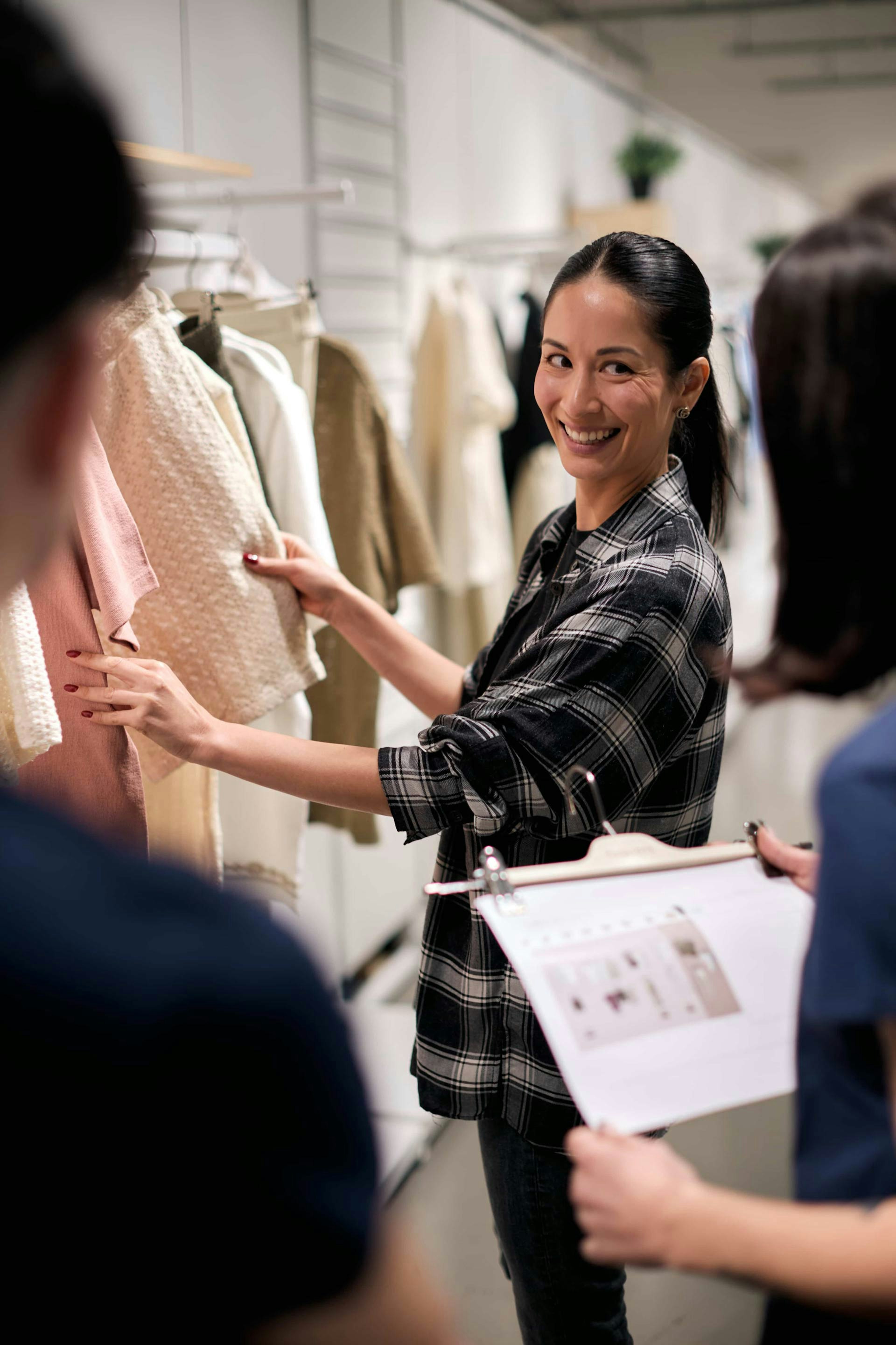 Personal shopper donna con camicia a quadri mostra capi d'abbigliamento beige a clienti in boutique