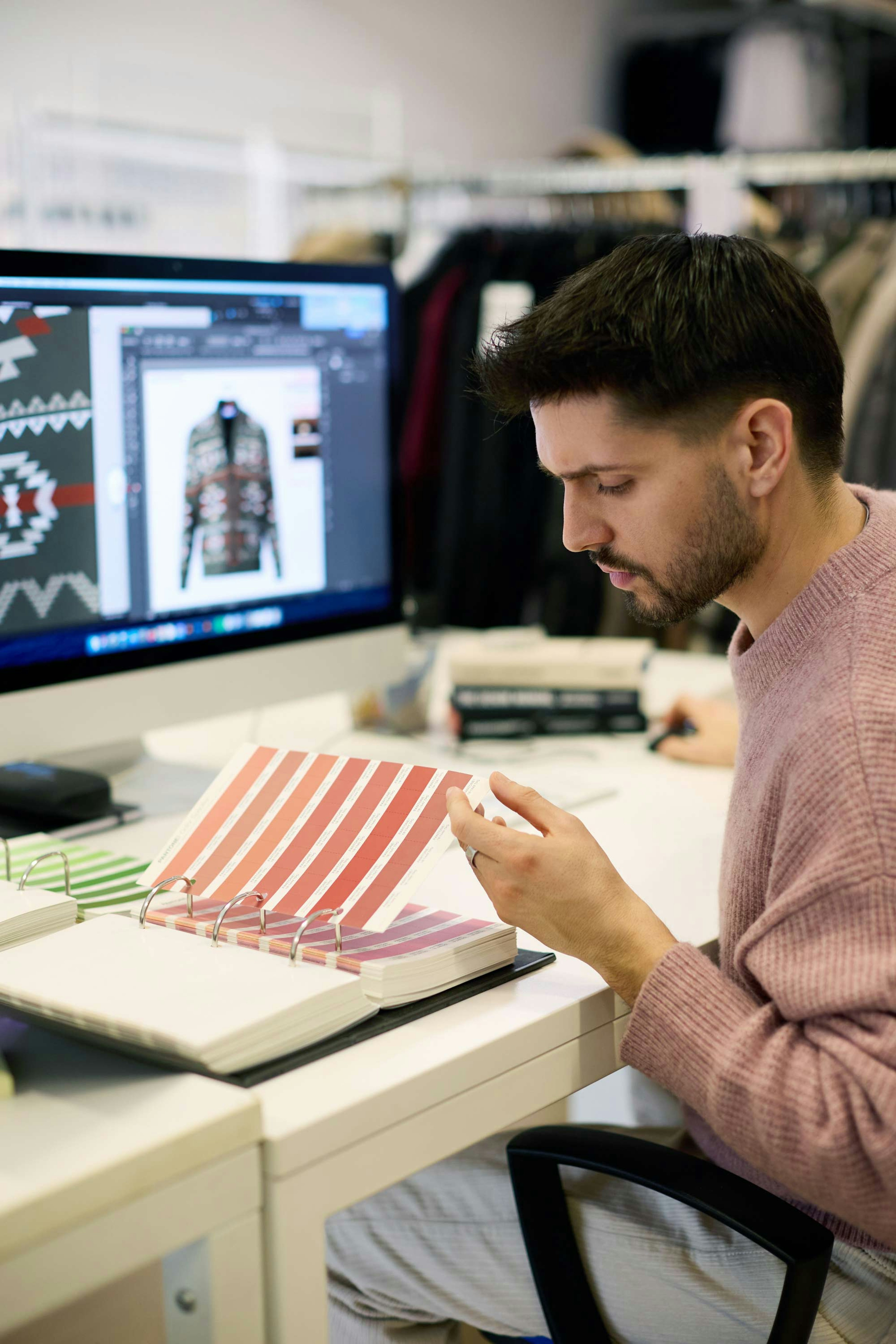 Designer di moda al lavoro con campioni di tessuto a righe rosa e computer con progetti di abbigliamento