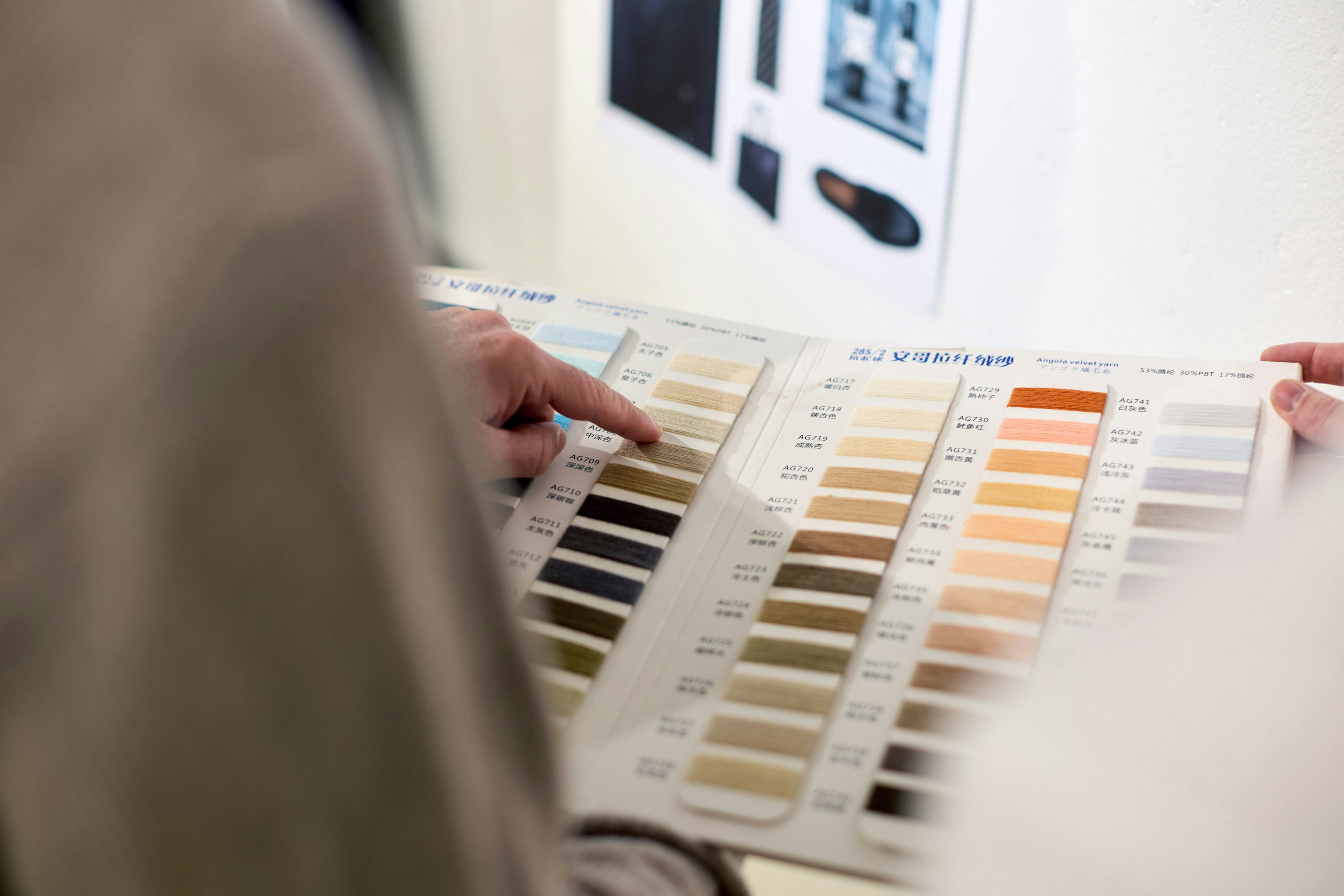 Mani che consultano un campionario professionale di colori e tessuti con codici di riferimento per la produzione tessile