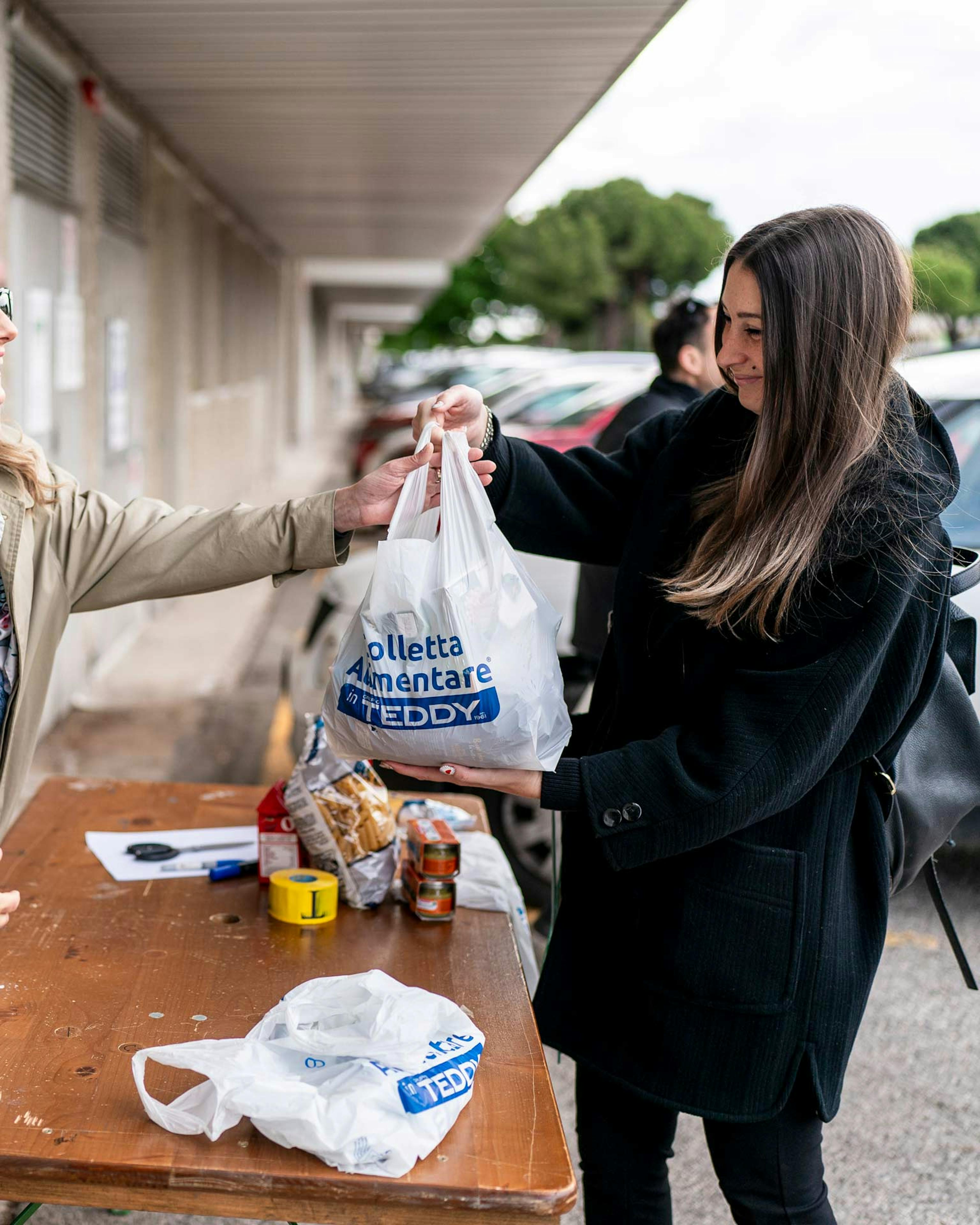 Volontaria distribuisce sacchetti della colletta alimentare Teddy durante iniziativa benefica aziendale all'aperto