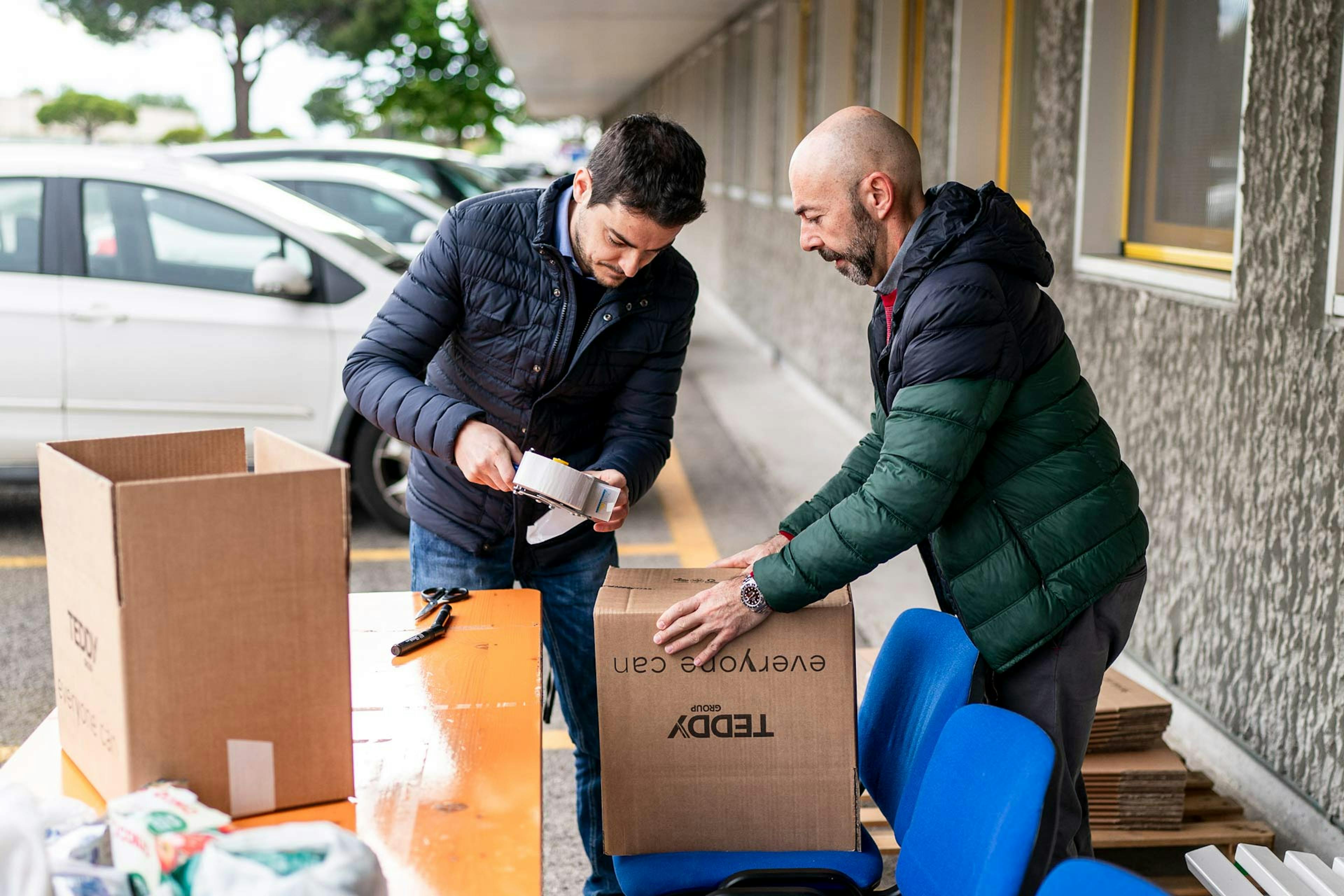 Due volontari preparano e imballano scatole di cartone per iniziativa benefica aziendale all'esterno della sede
