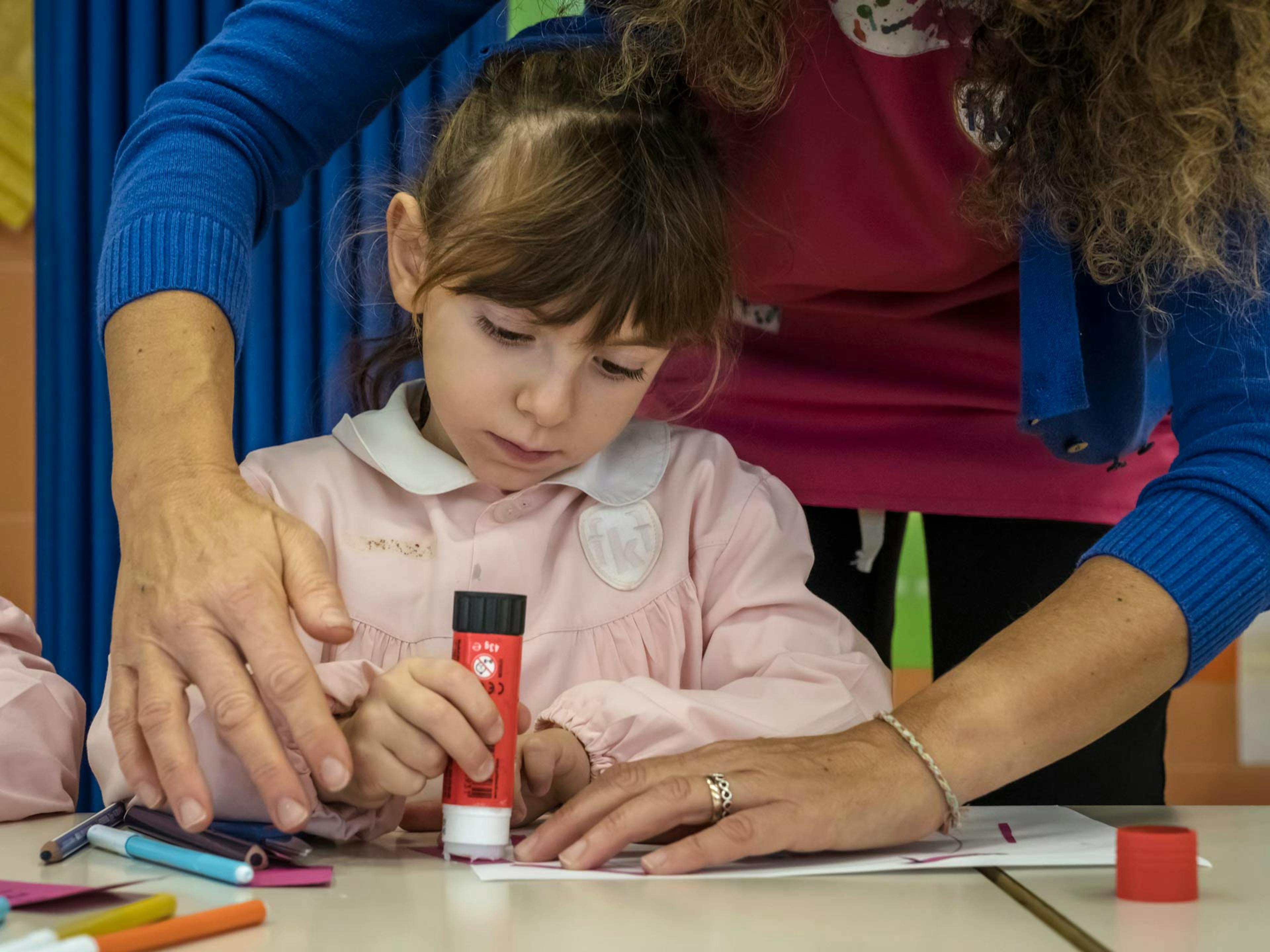 Bambina concentrata durante laboratorio creativo di disegno con pennarelli colorati, supportata da educatrici