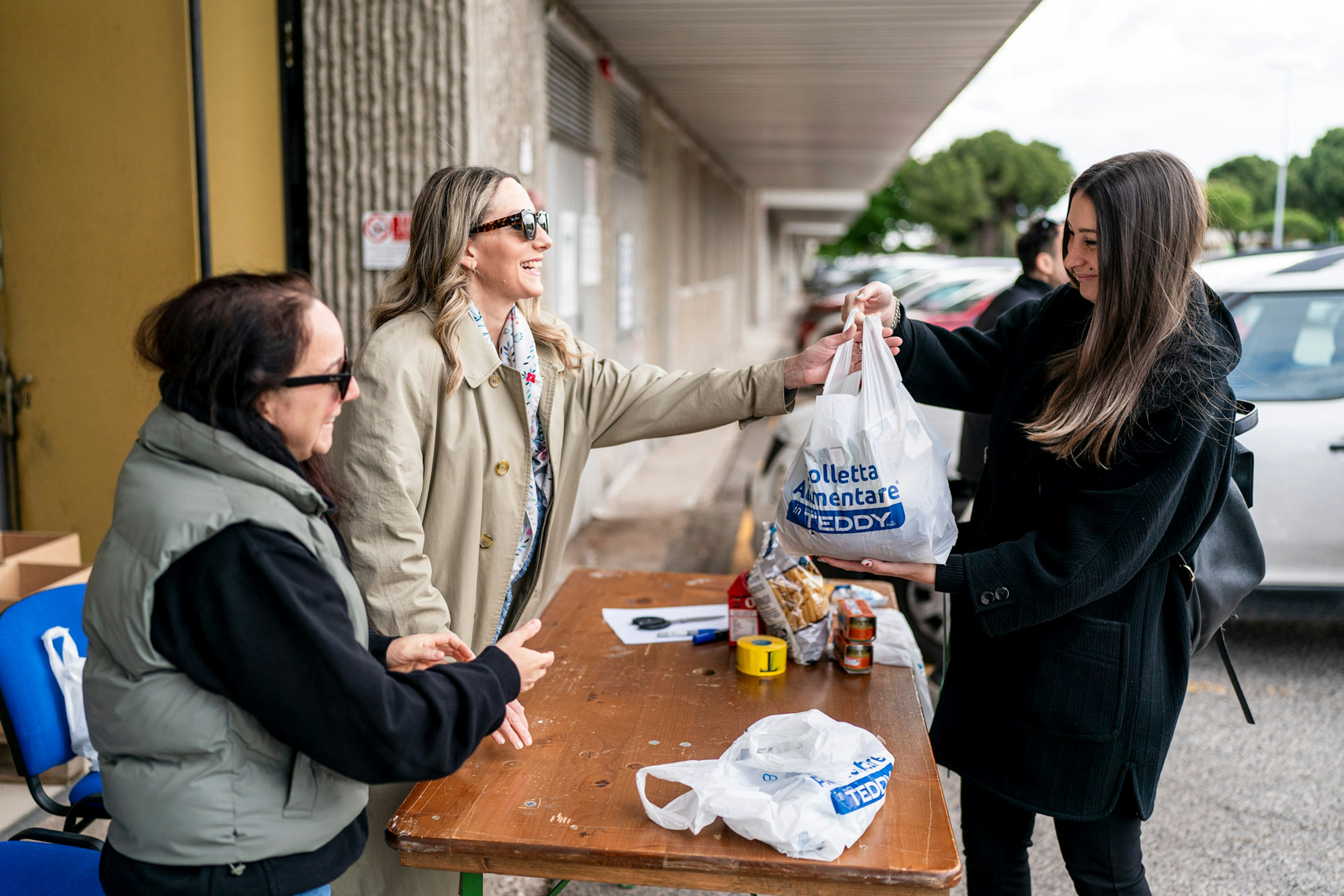 Volontarie distribuiscono borse della spesa con logo Teddy durante giornata di colletta alimentare aziendale