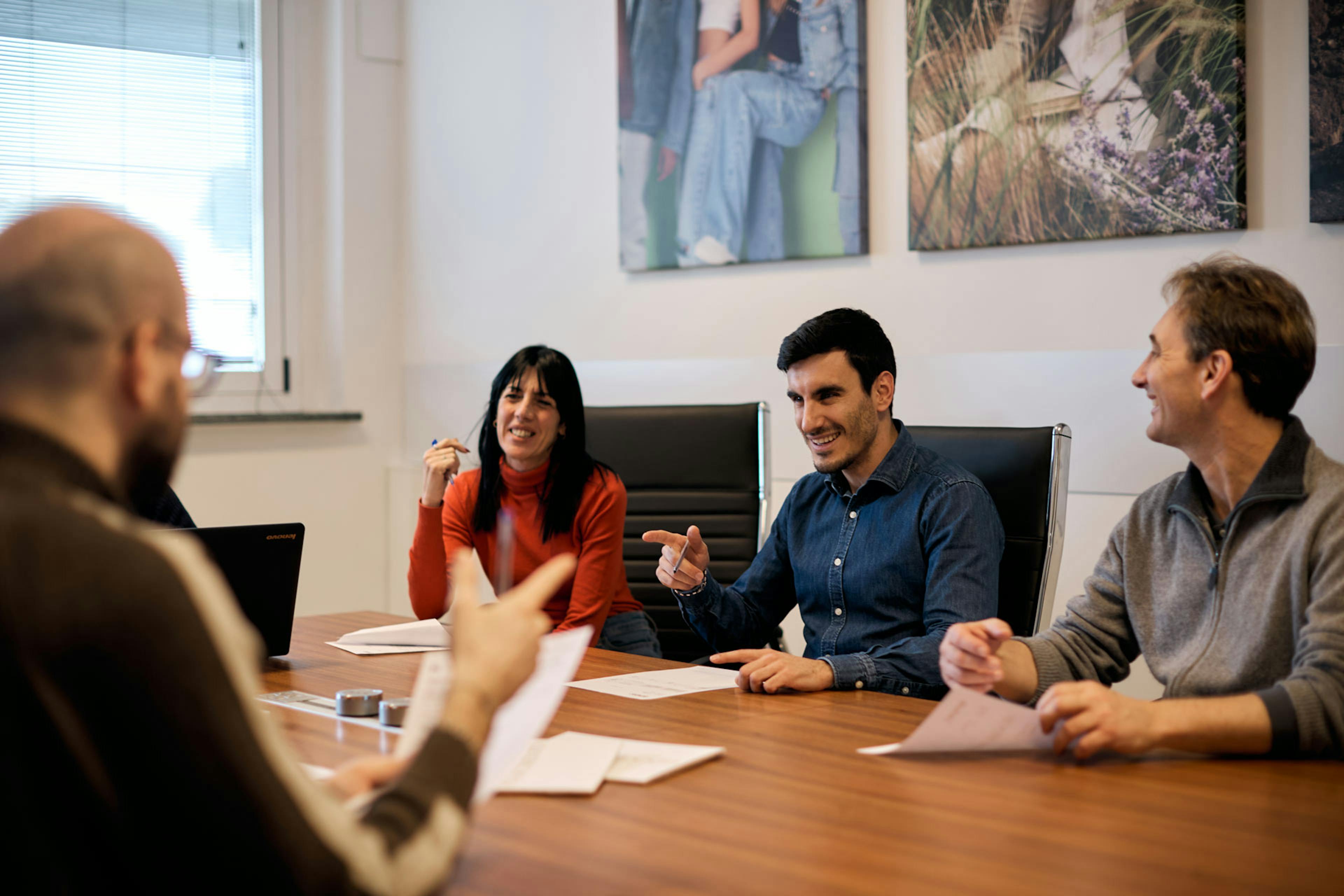Team di quattro persone durante riunione collaborativa in sala meeting aziendale con tavolo in legno