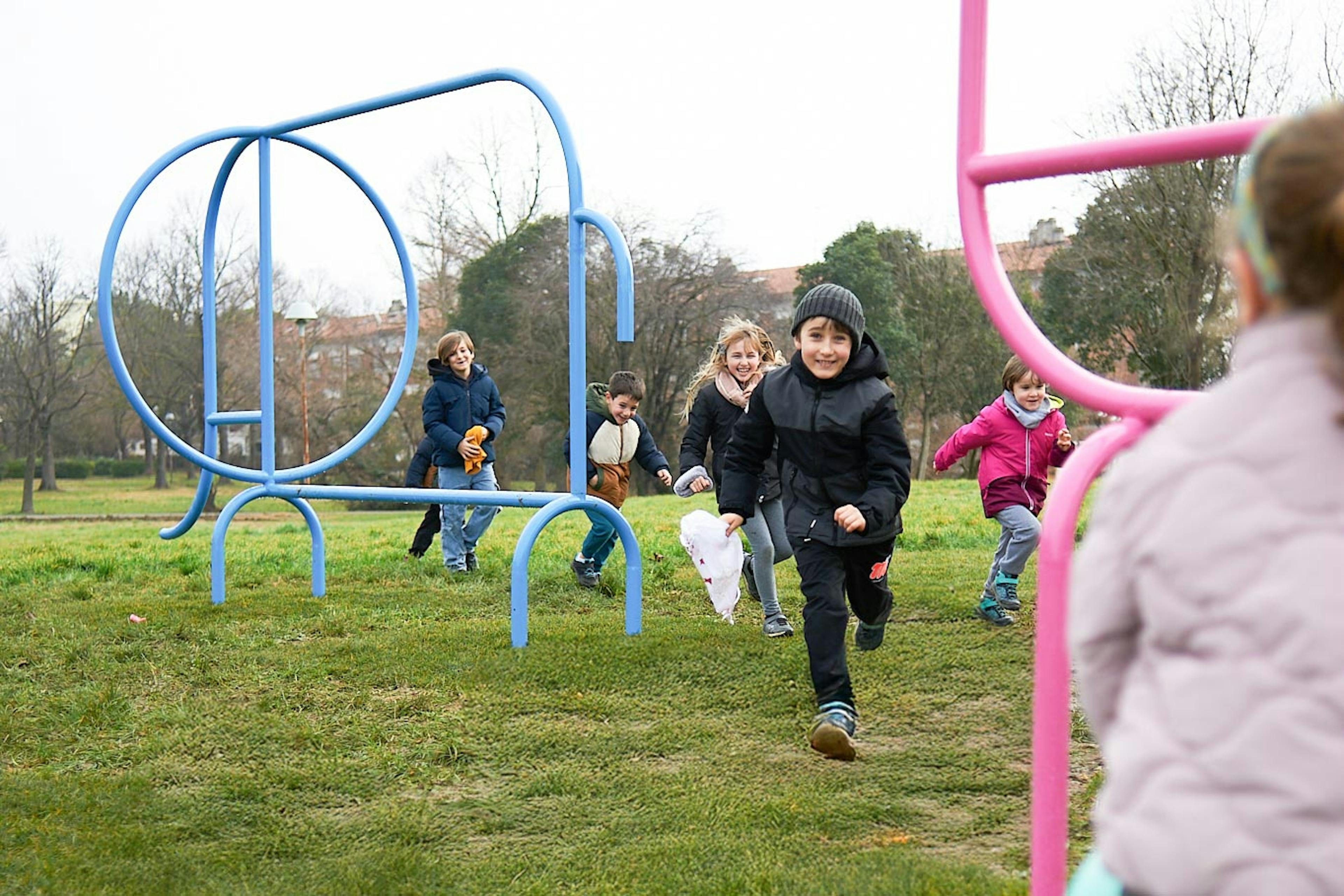 Gruppo di bambini corre felice su prato verde con attrezzature colorate del parco giochi pubblico