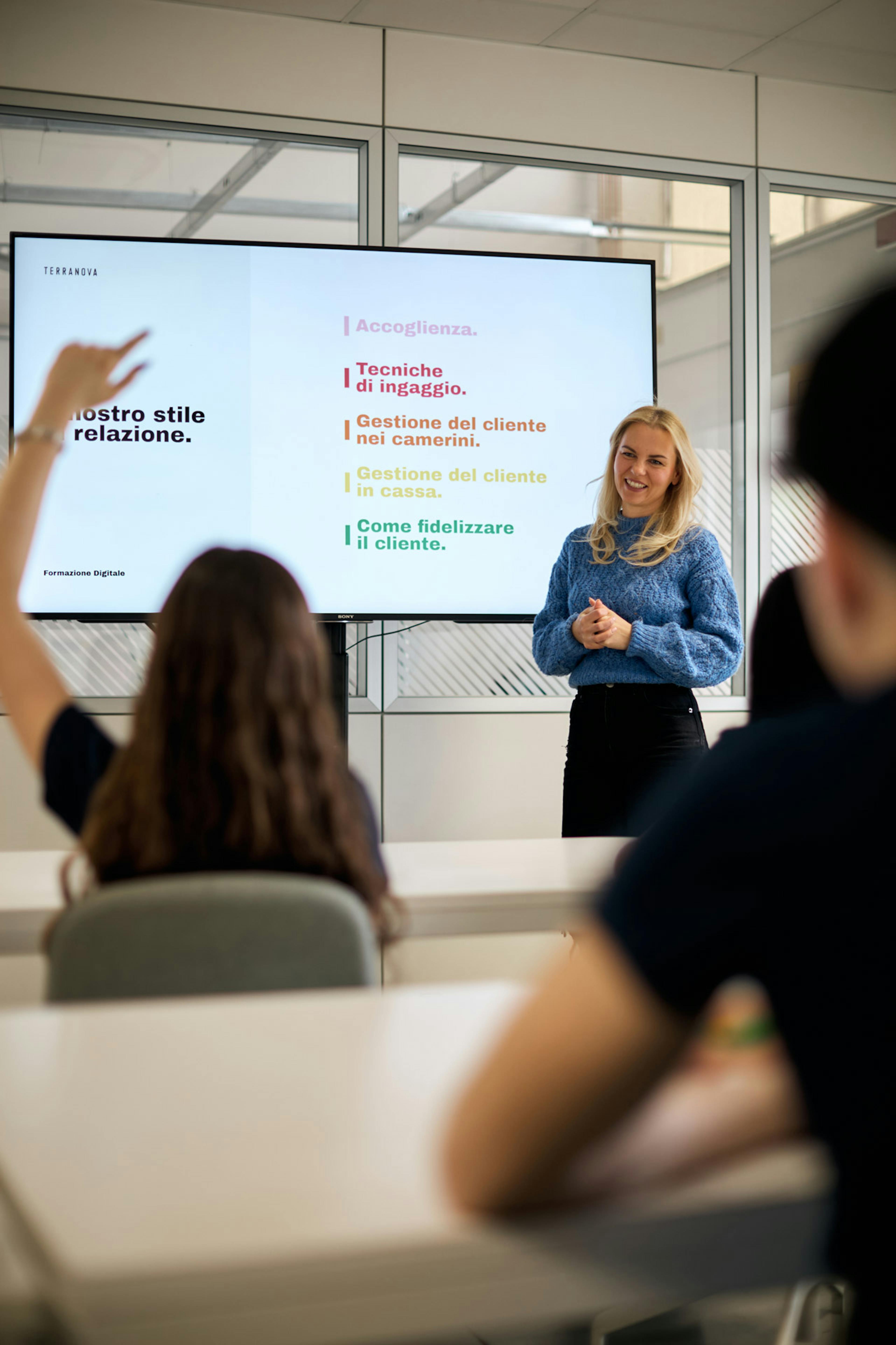 Formatrice presenta corso di formazione digitale su tecniche di accoglienza e gestione cliente con slide proiettate