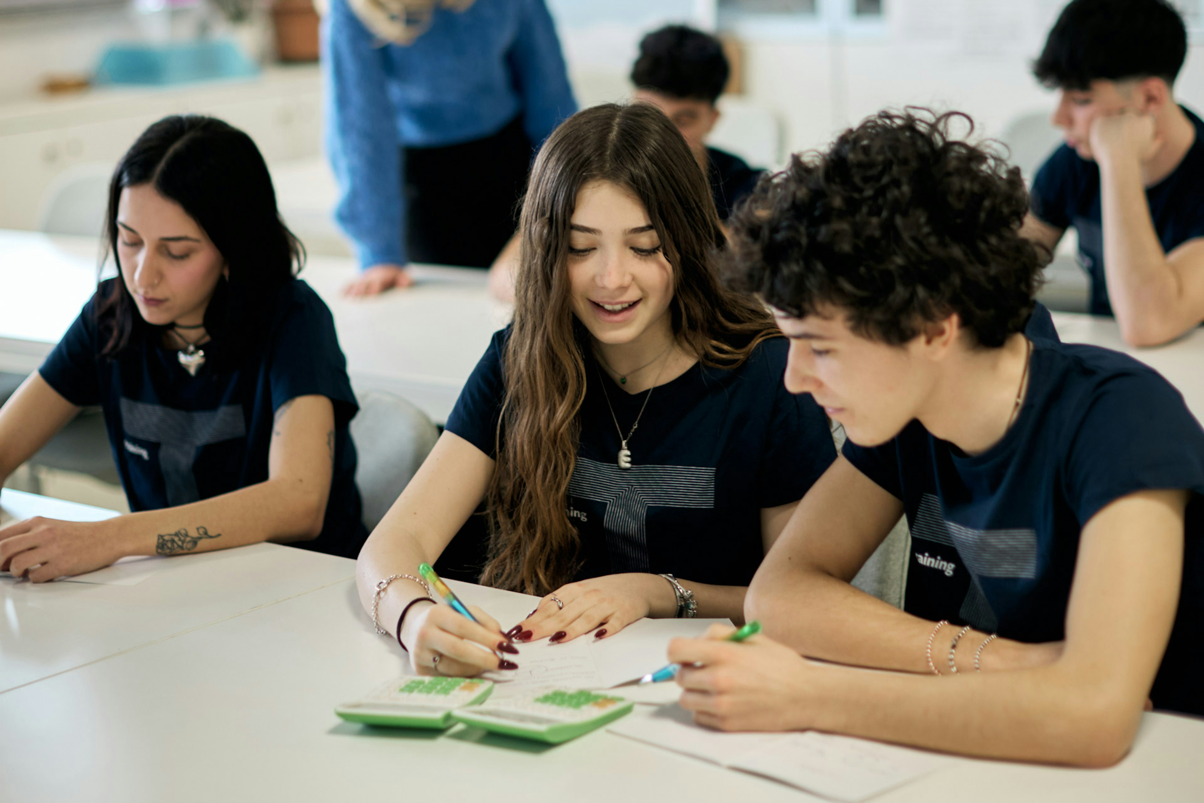 Giovani studenti in maglietta nera collaborano su progetto di design con supervisione formatrice in aula moderna