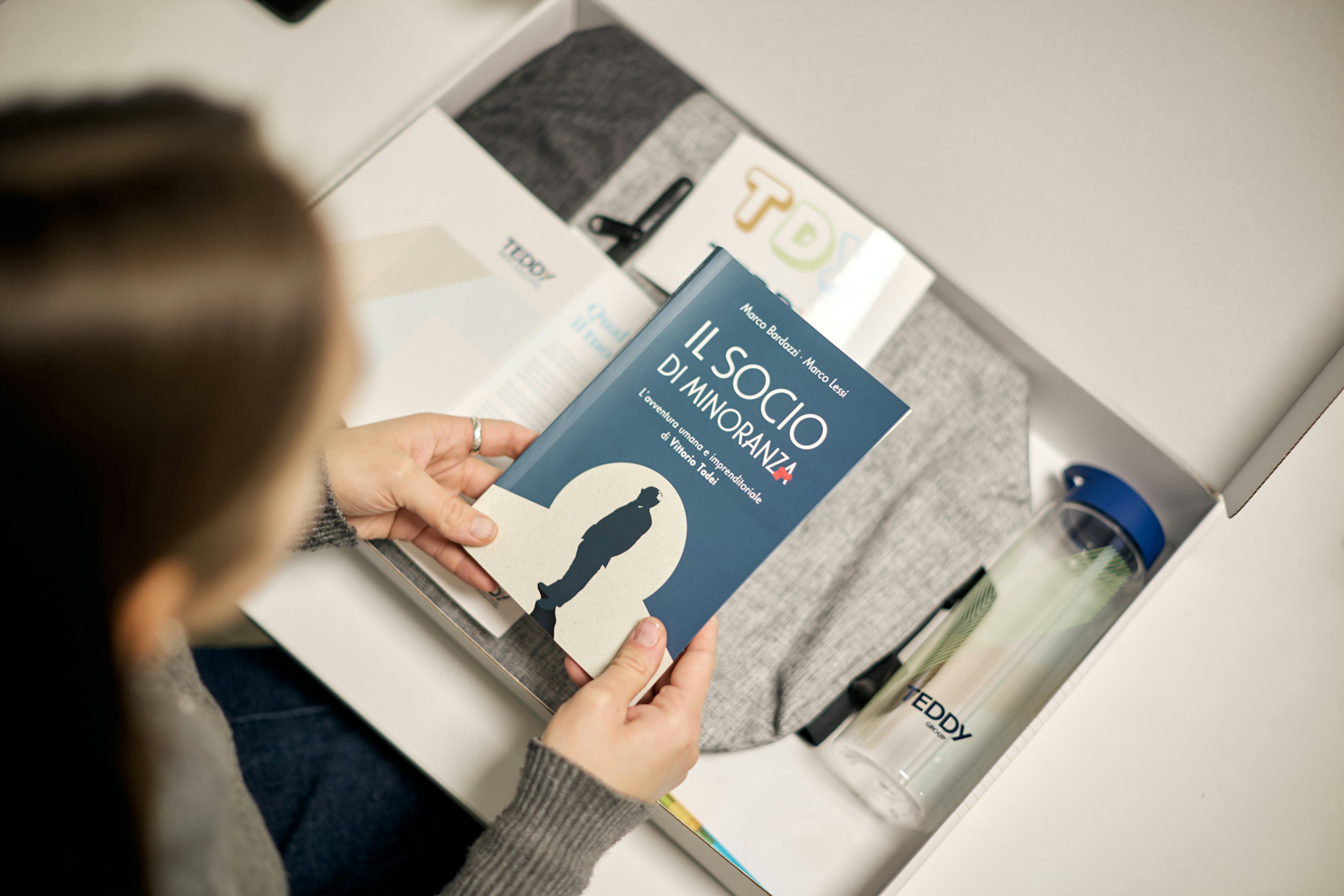Donna apre confezione contenente libro 'Il socio di minoranza' di Teddy con altri prodotti del brand visibili nel packaging