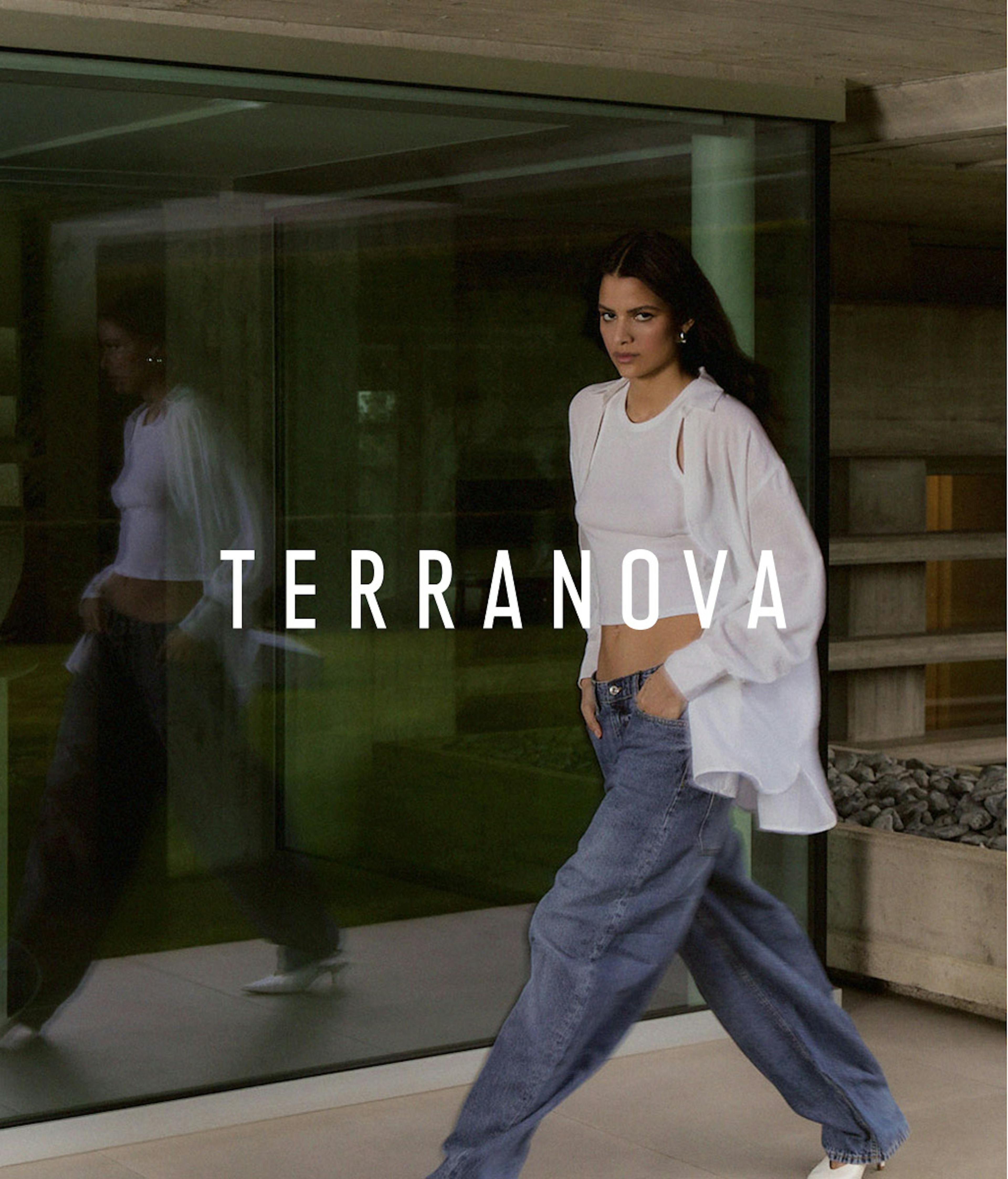 Modella con capelli scuri che indossa un completo casual bianco composto da crop top e cardigan abbinato a jeans larghi, fotografata davanti a una vetrata moderna. Il nome del brand Terranova è visualizzato in testo bianco