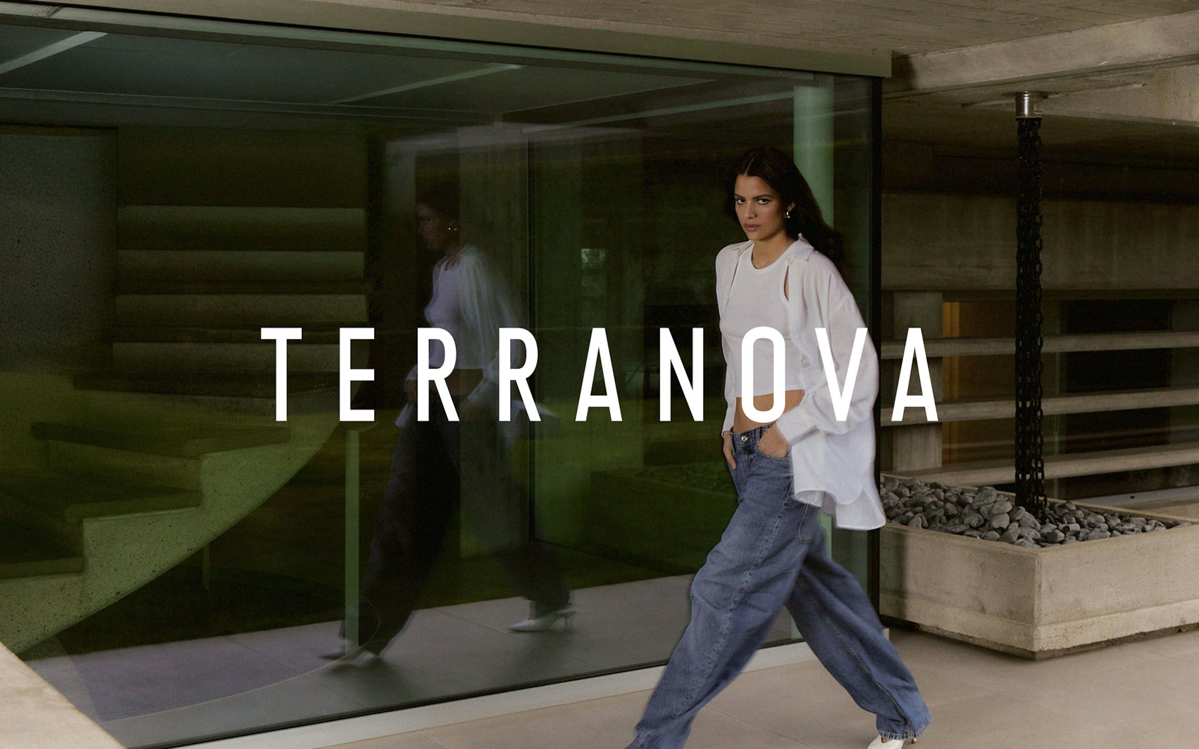 Modella con capelli scuri che indossa un completo casual bianco composto da crop top e cardigan abbinato a jeans larghi, fotografata davanti a una vetrata moderna. Il nome del brand Terranova è visualizzato in testo bianco