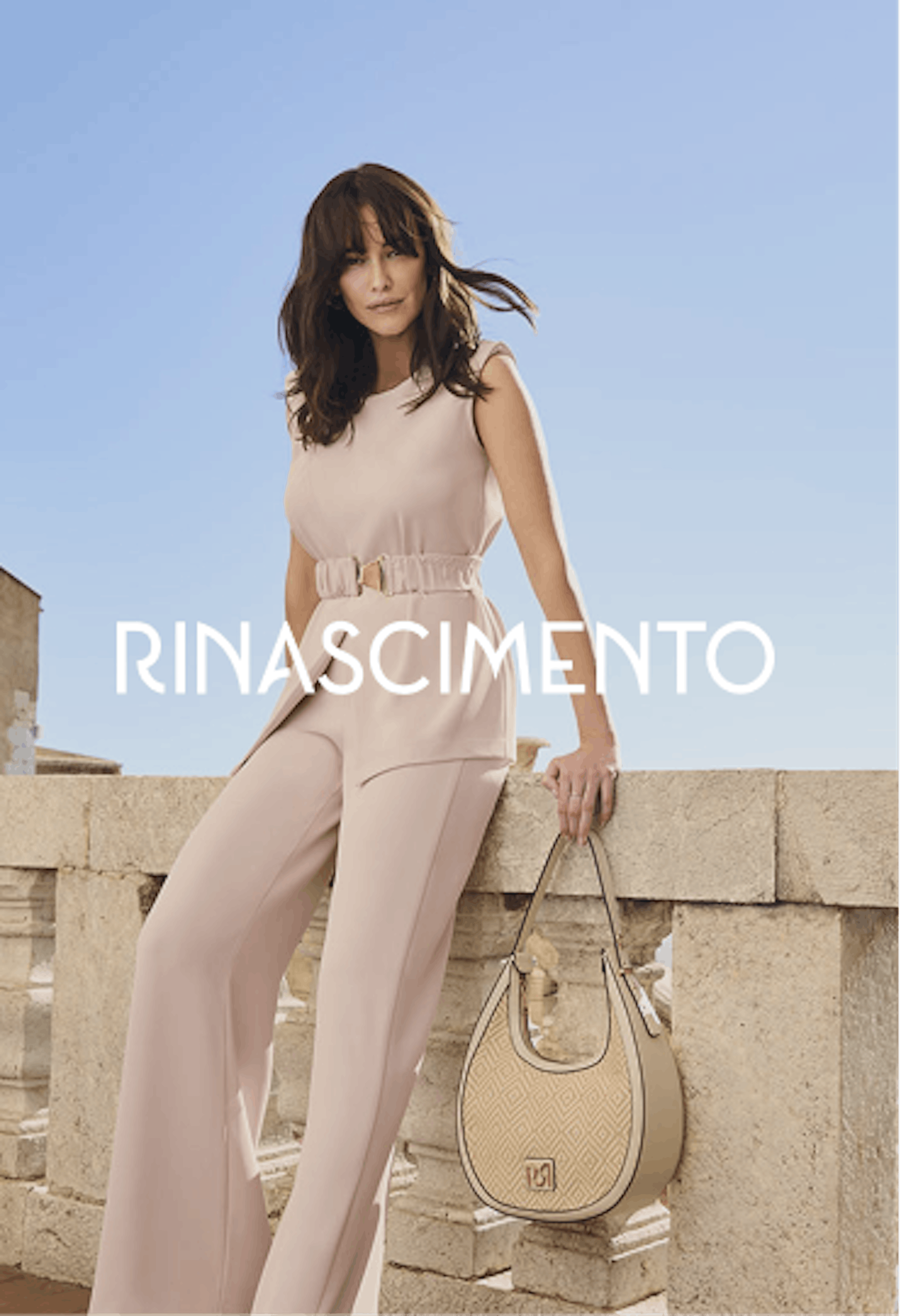 Modella in elegante completo beige composto da top senza maniche e pantaloni a gamba larga con cintura, che tiene una borsa beige, in posa contro elementi architettonici in pietra. Il nome Rinascimento appare in lettere bianche