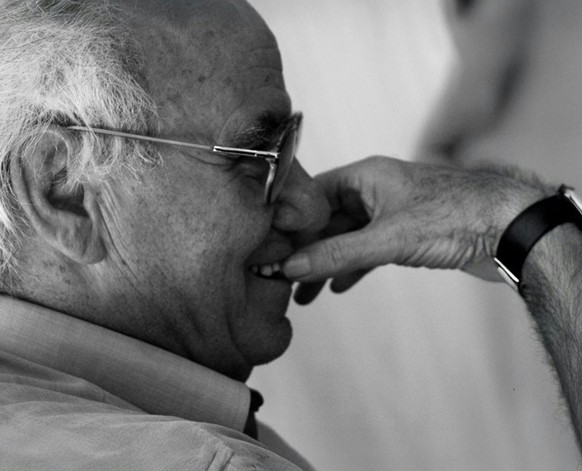 Ritratto in bianco e nero di Vittorio Tadei con occhiali che si porta la mano al viso in un gesto contemplativo. L'immagine presenta elementi grafici lineari sovrapposti che creano un effetto visivo dinamico