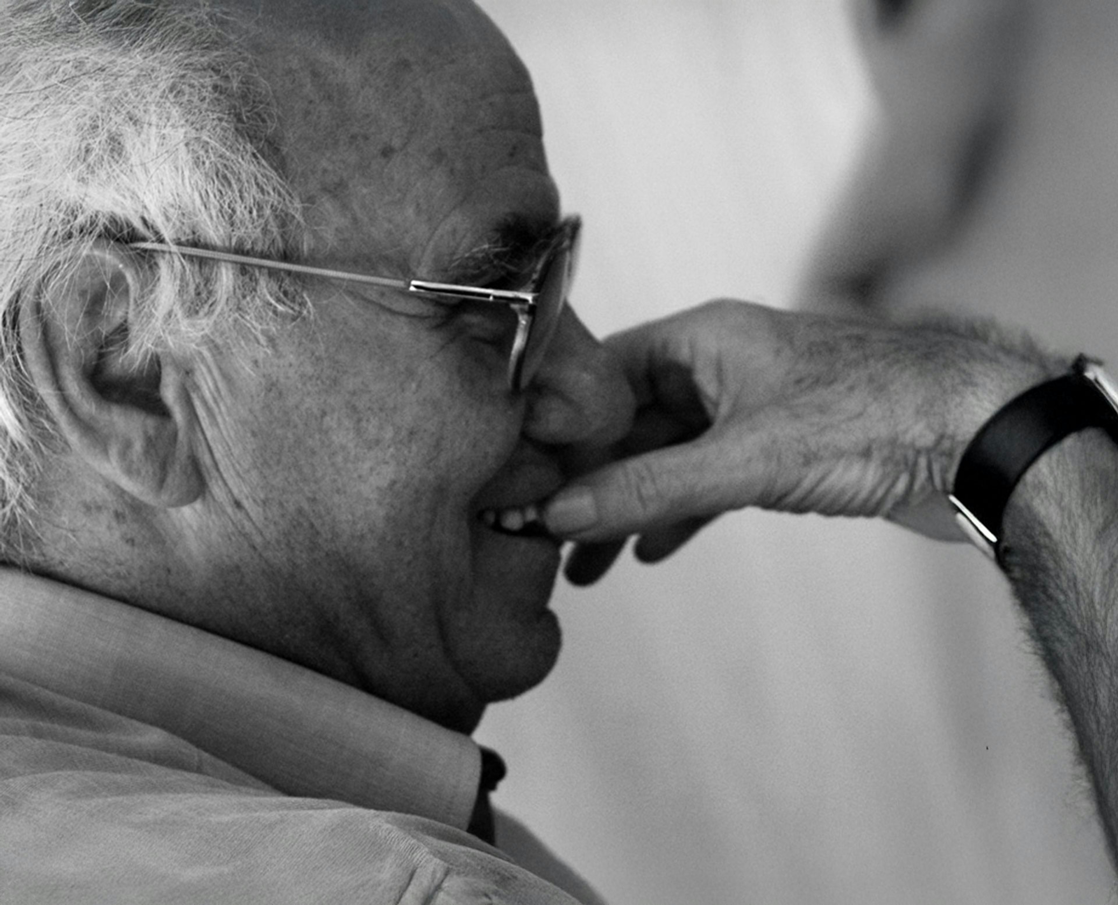 Ritratto in bianco e nero di Vittorio Tadei con occhiali che si porta la mano al viso in un gesto contemplativo. L'immagine presenta elementi grafici lineari sovrapposti che creano un effetto visivo dinamico