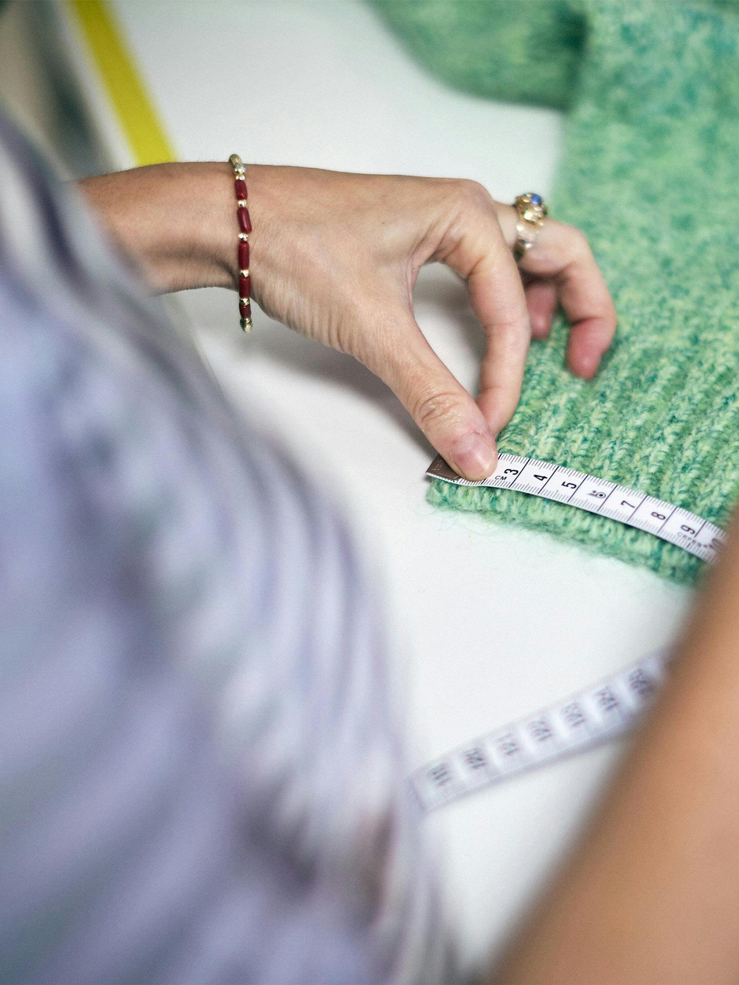 Sarta che misura tessuto verde texture con metro da sarta su tavolo da lavoro, attività di taglio e cucito