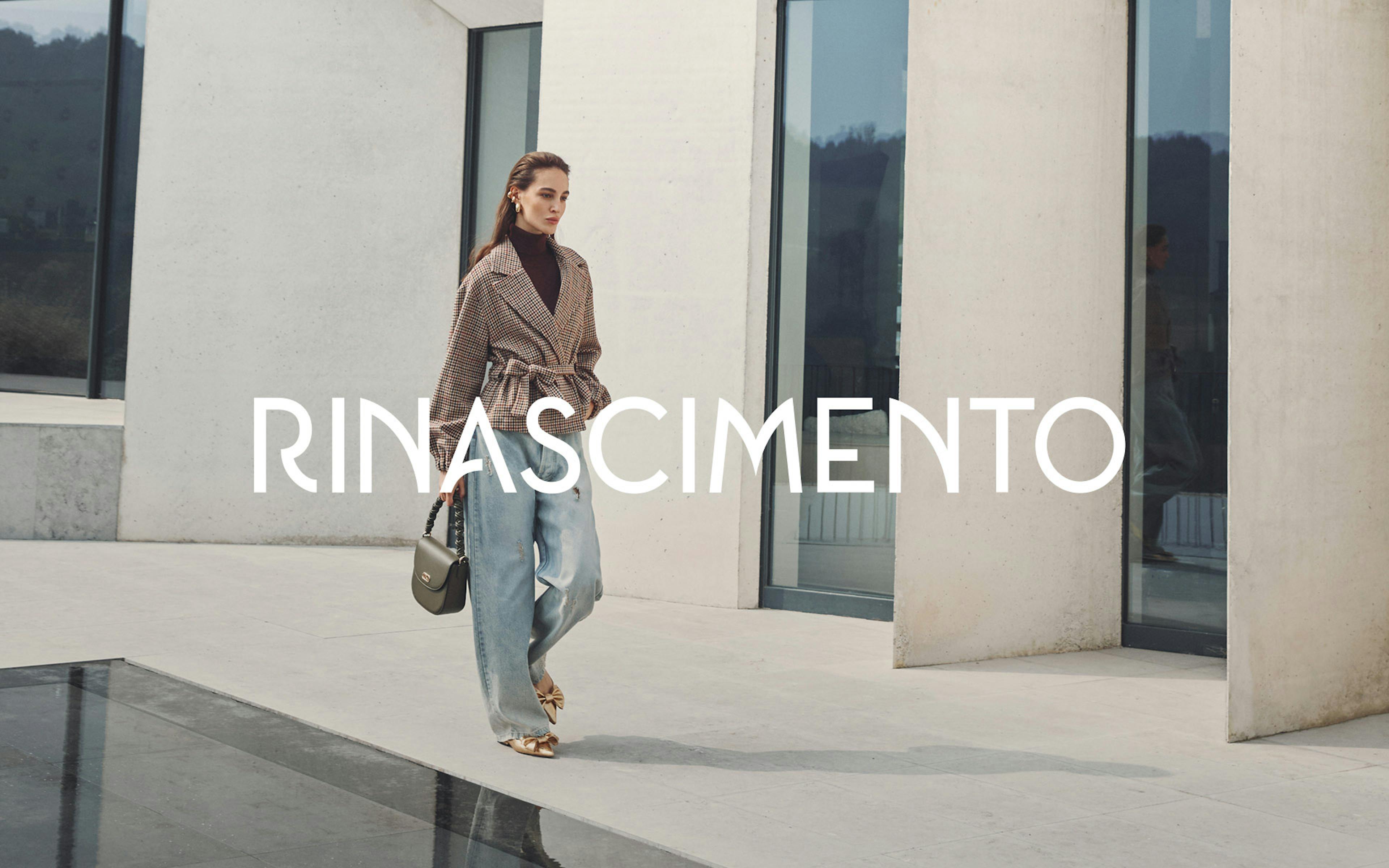 Modella in elegante completo beige composto da top senza maniche e pantaloni a gamba larga con cintura, che tiene una borsa beige, in posa contro elementi architettonici in pietra. Il nome Rinascimento appare in lettere bianche