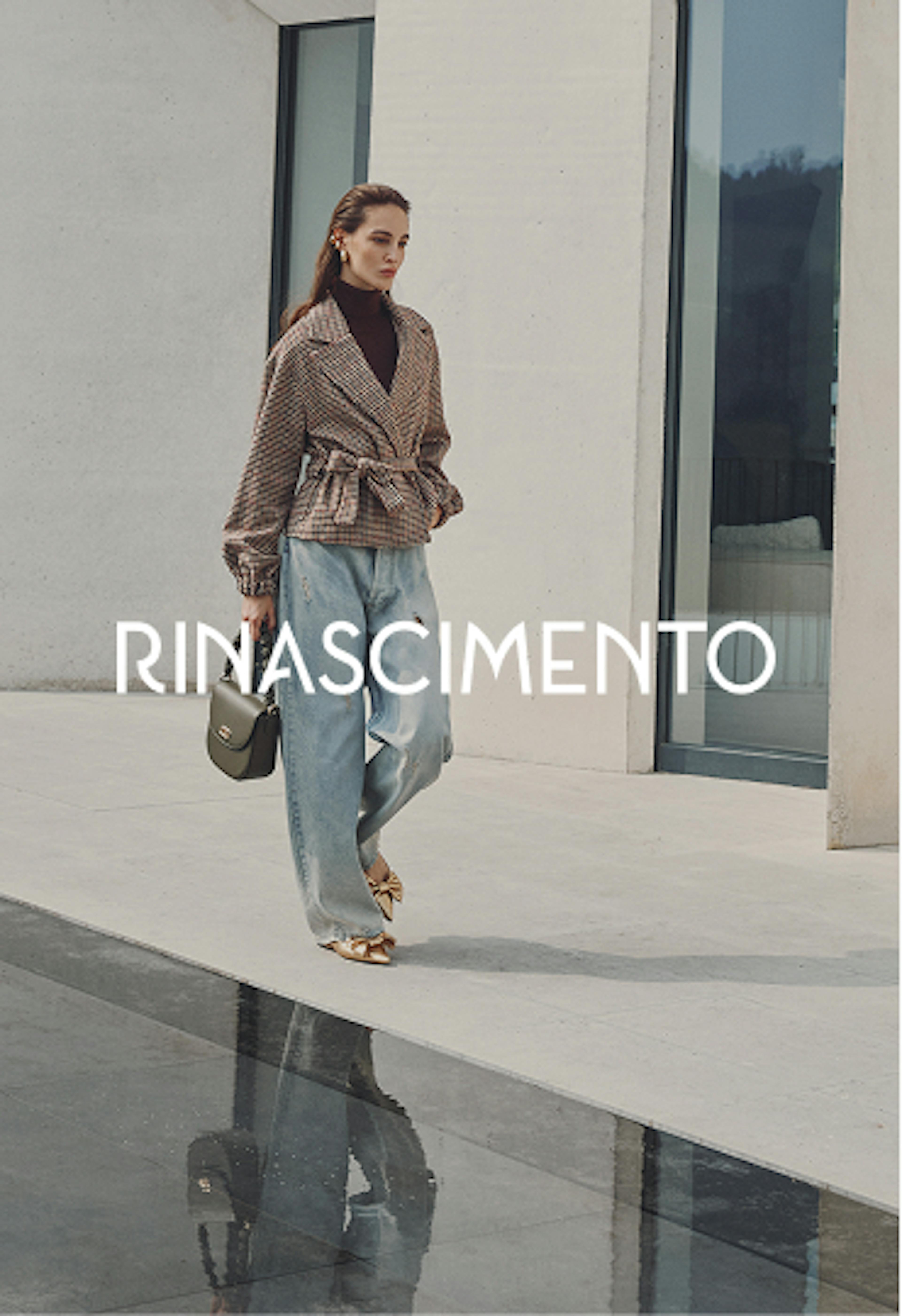 Modella in elegante completo beige composto da top senza maniche e pantaloni a gamba larga con cintura, che tiene una borsa beige, in posa contro elementi architettonici in pietra. Il nome Rinascimento appare in lettere bianche