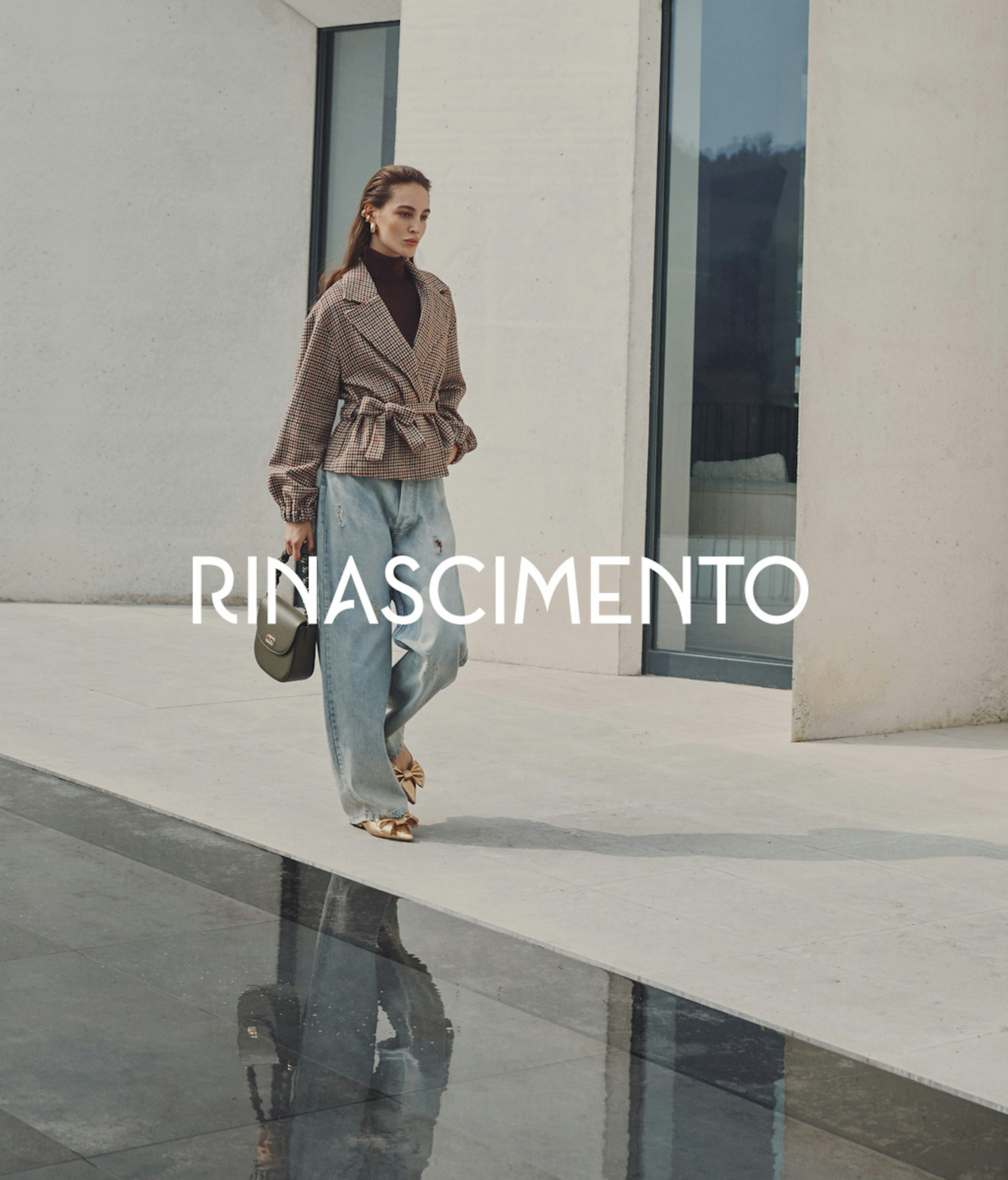 Modella in elegante completo beige composto da top senza maniche e pantaloni a gamba larga con cintura, che tiene una borsa beige, in posa contro elementi architettonici in pietra. Il nome Rinascimento appare in lettere bianche