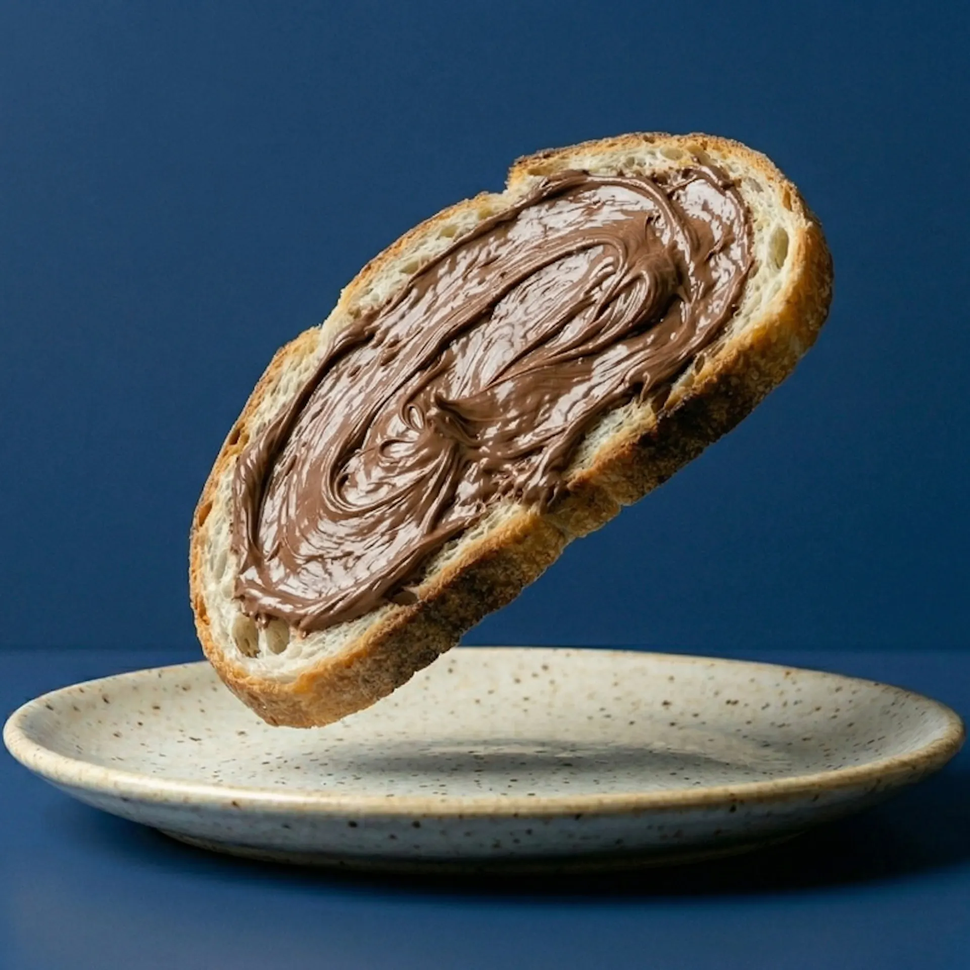 Una fetta di pane con la Nutella, sospesa su un piatto bianco