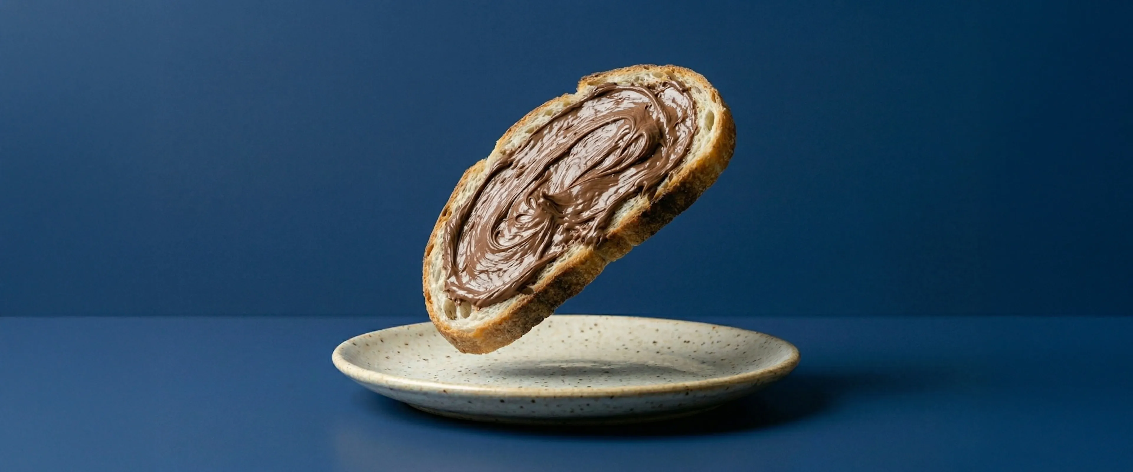 Una fetta di pane con la Nutella, sospesa su un piatto bianco