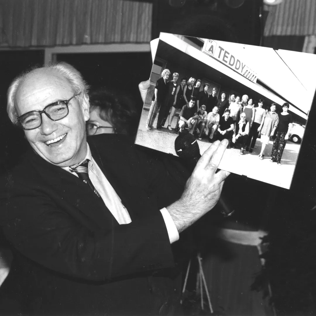 Foto in bianco e nero di Vittorio Tadei che mostra una foto stampata del team di Teddy sotto l'insegna dell'azienda