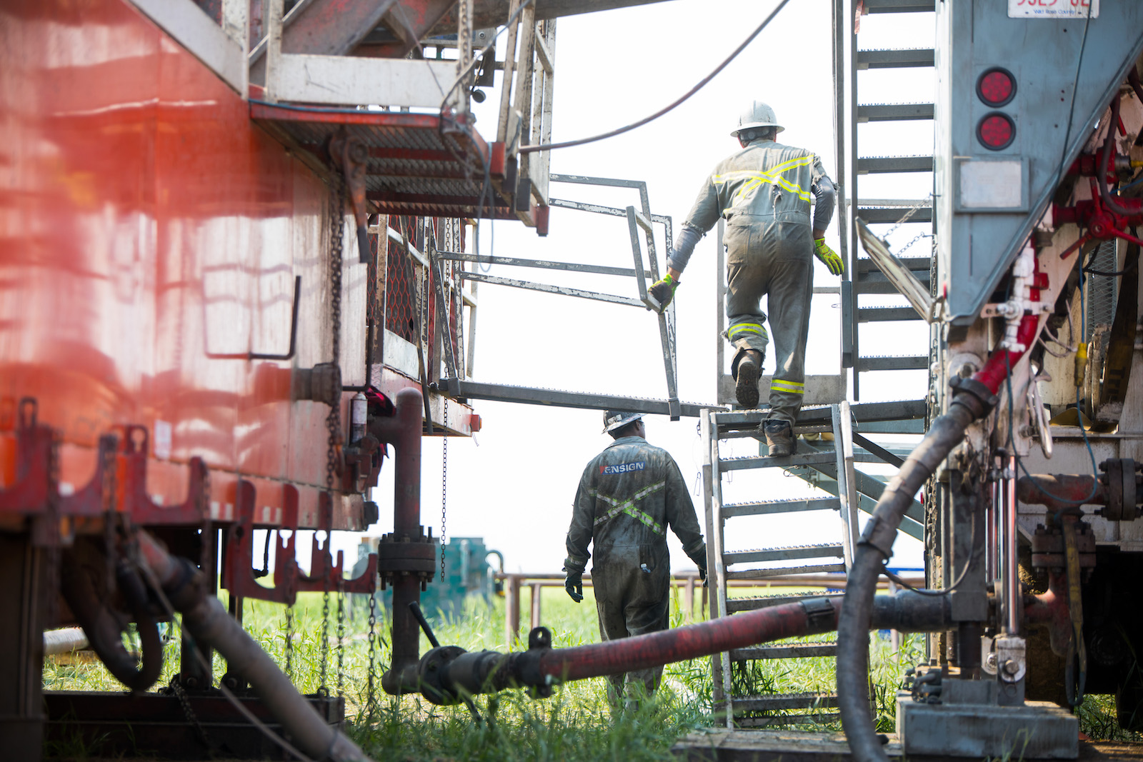 Two oil workers at work on a ladder and the ground.