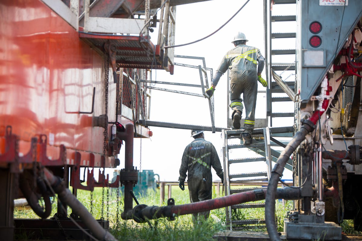 Two oil workers at work on a ladder and the ground.