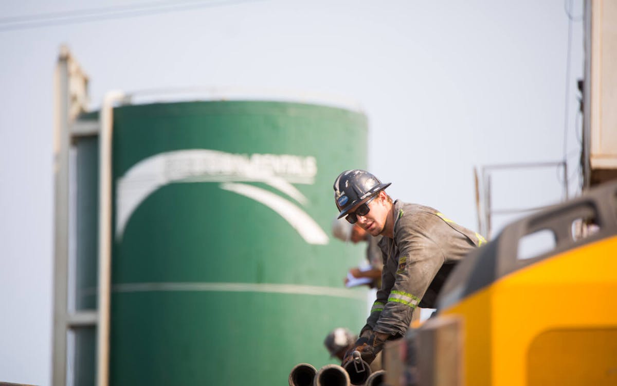 A worker in a brown uniform, sunglasses and a hard hat works on an oil rig.