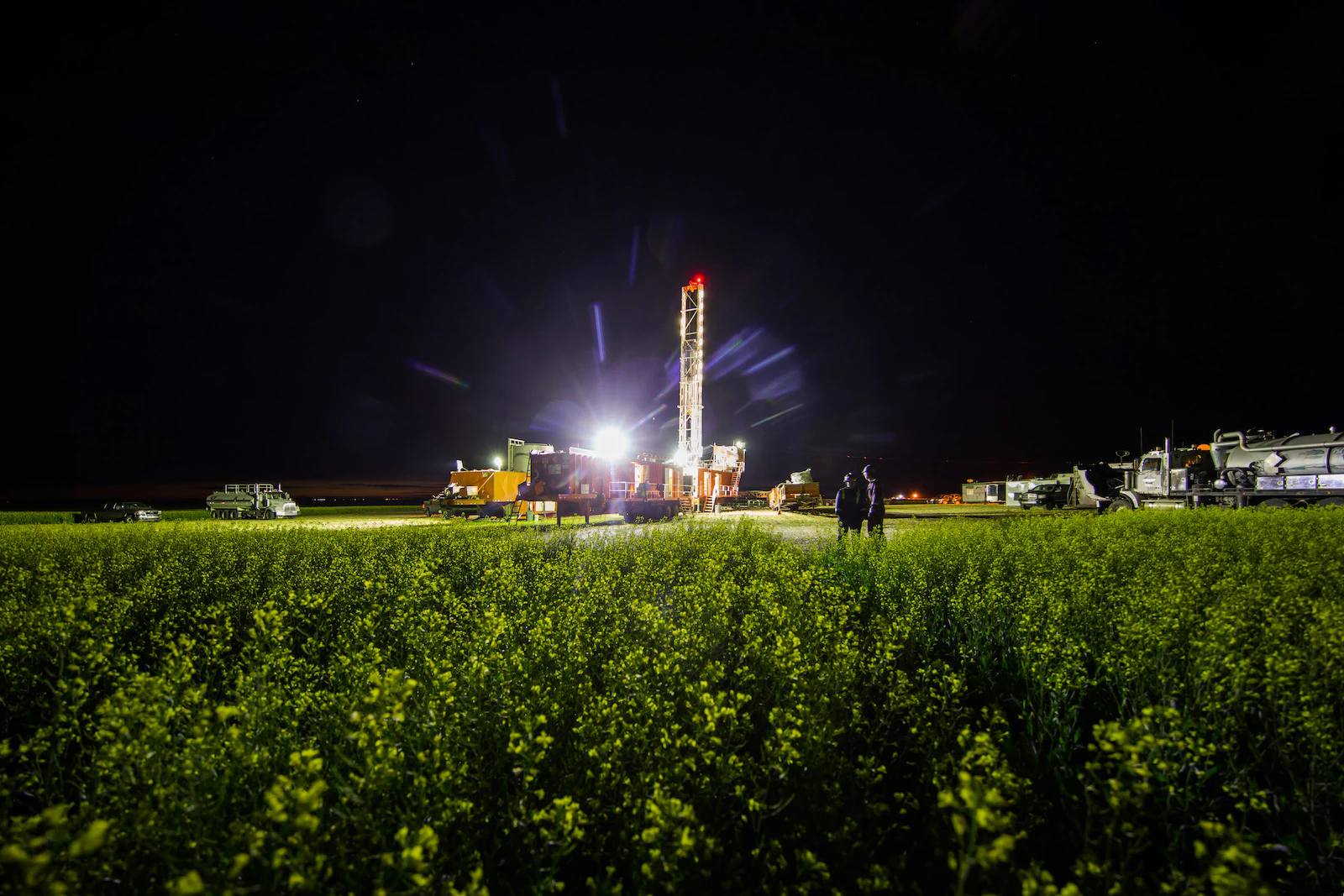 An oil rig at night, backlit by a bright light.