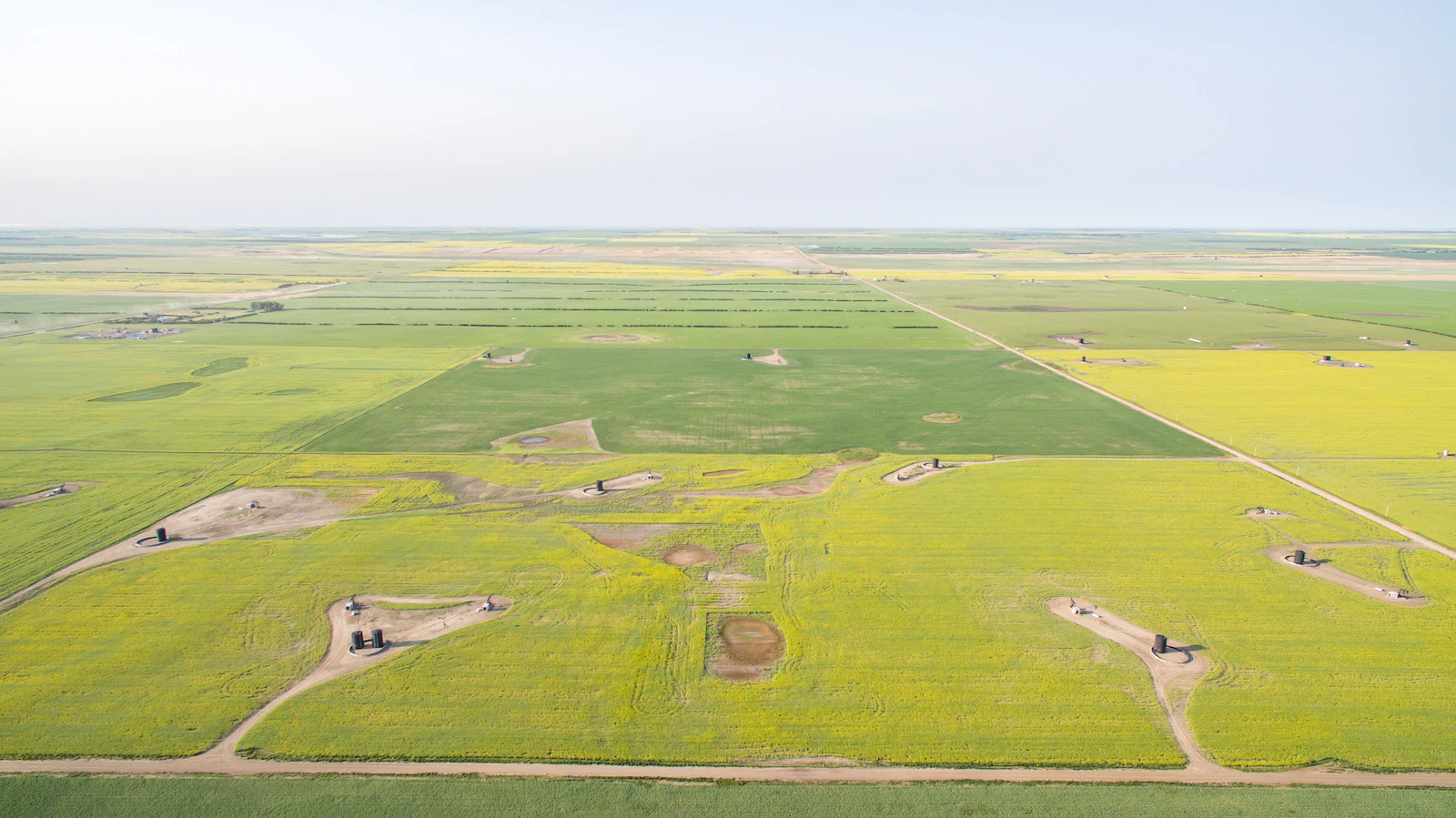 An aerial view of wide-open fields under a blue sky, dotted with oil equipment.