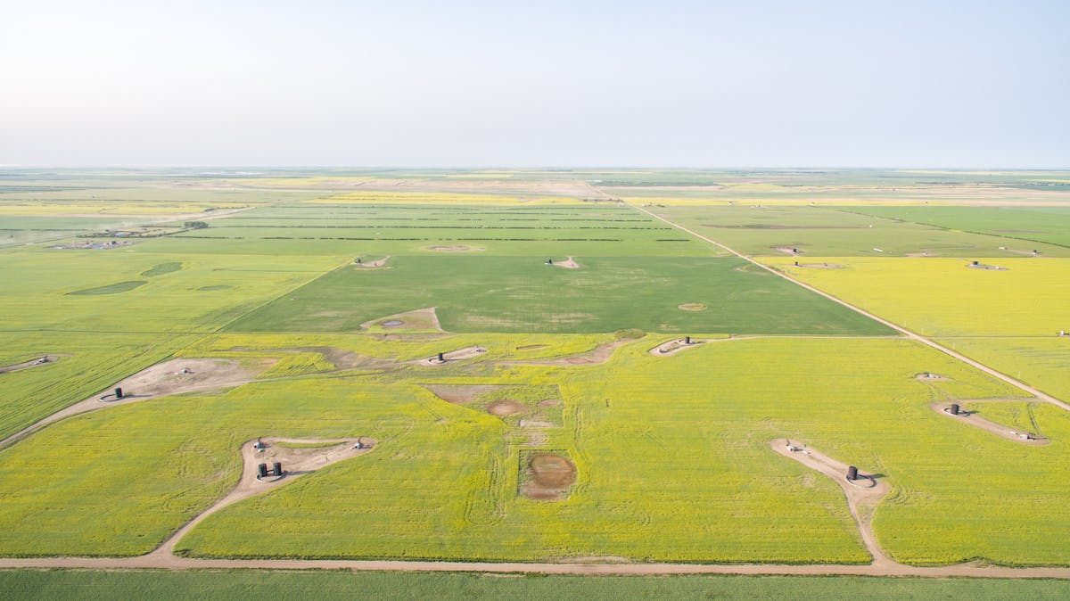An aerial view of wide-open fields under a blue sky, dotted with oil equipment.