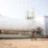 An oil worker walking with a clipboard, in front of a large white tank.