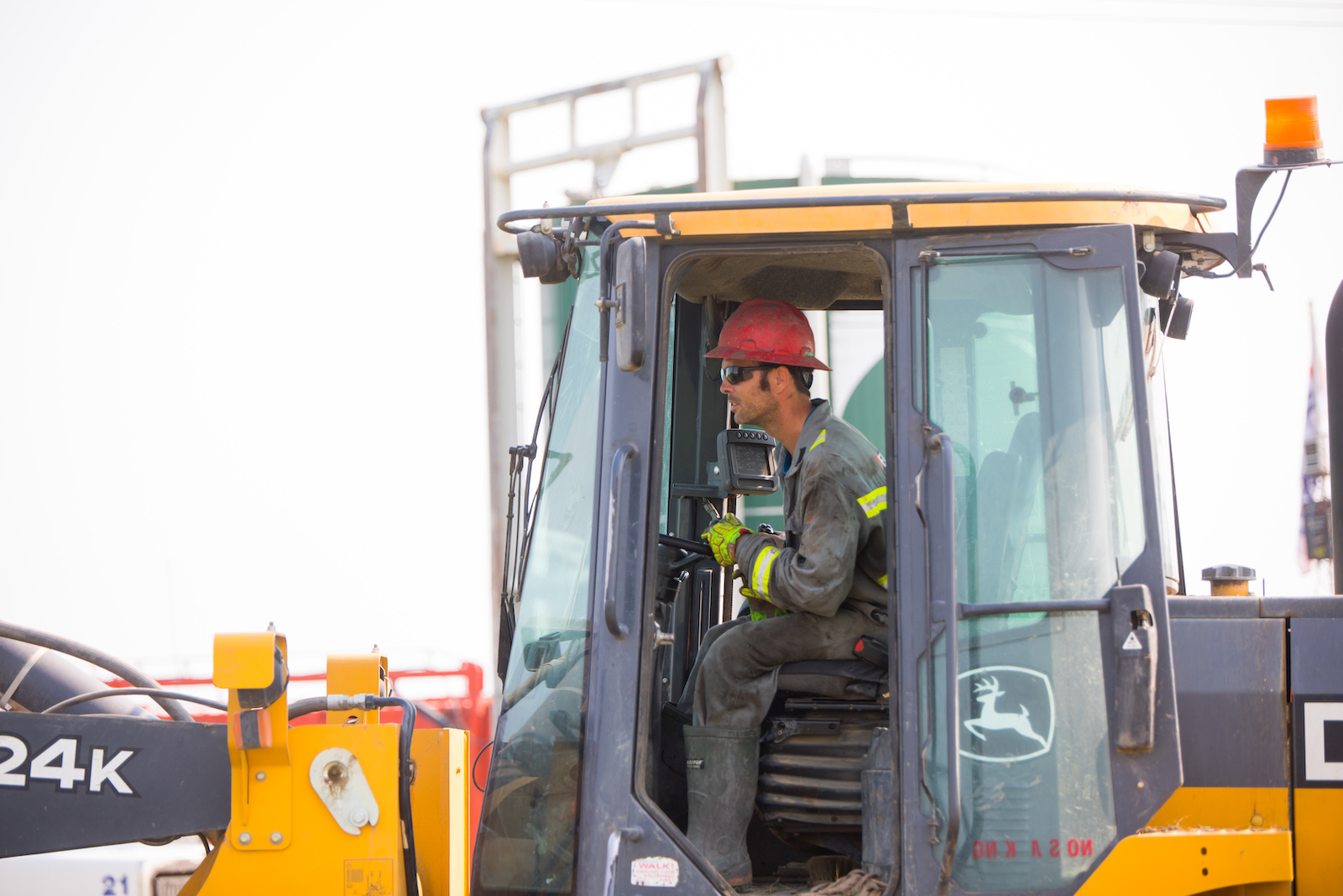 An oil worker wearing a red hard hat drives a tractor.