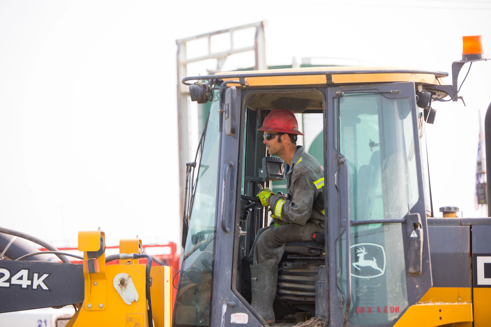 An oil worker wearing a red hard hat drives a tractor.