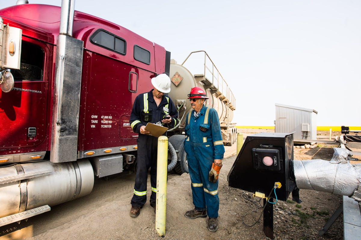 Two oil workers discussing the contents of a clipboard, next to a red truck.