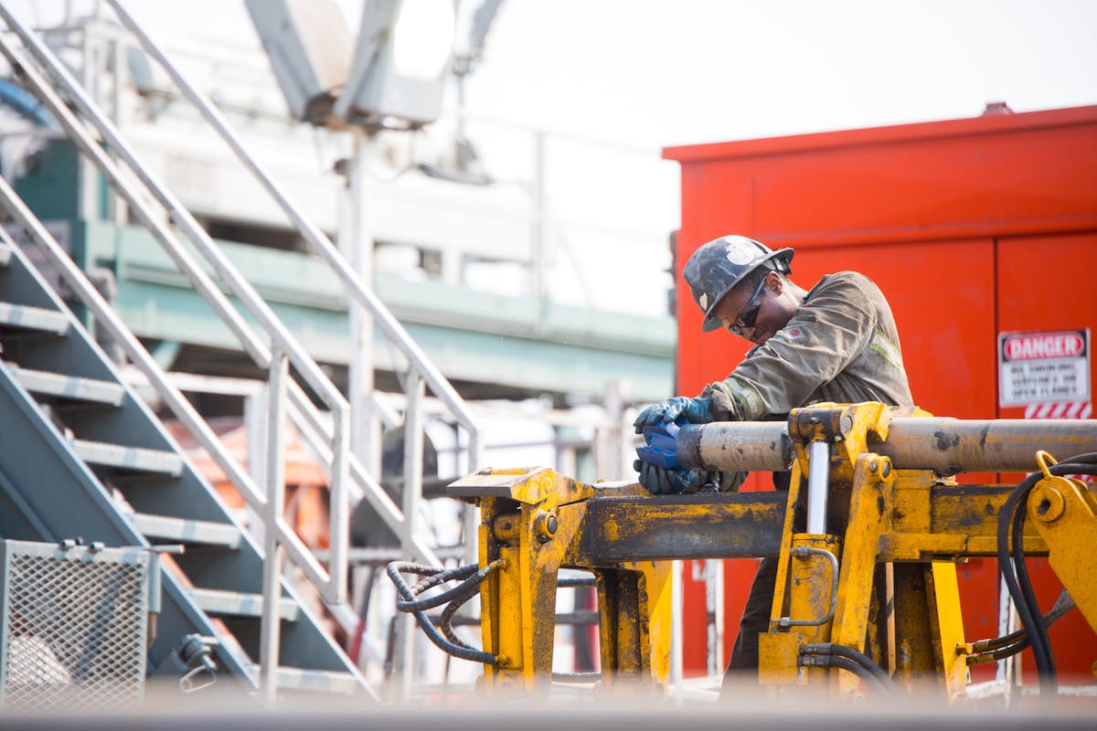 An oil rig worker fits a pipe near a danger sign.