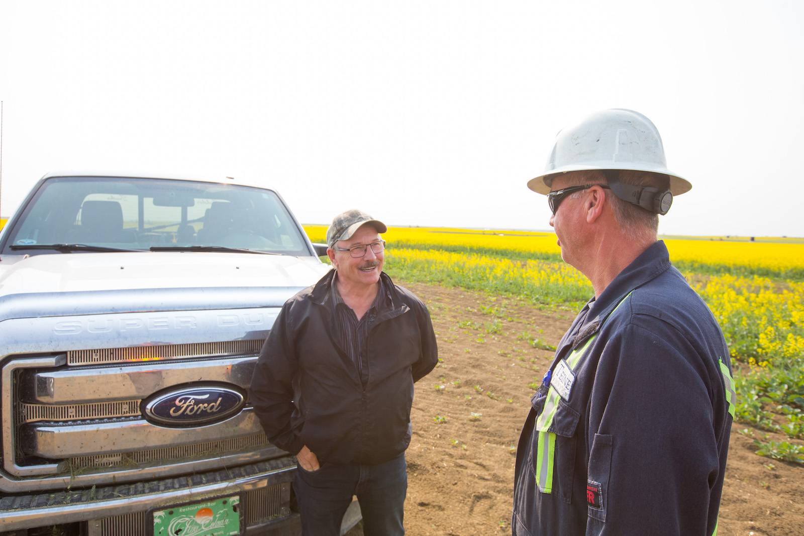 A farmer and an oil worker chat next to a Ford truck.