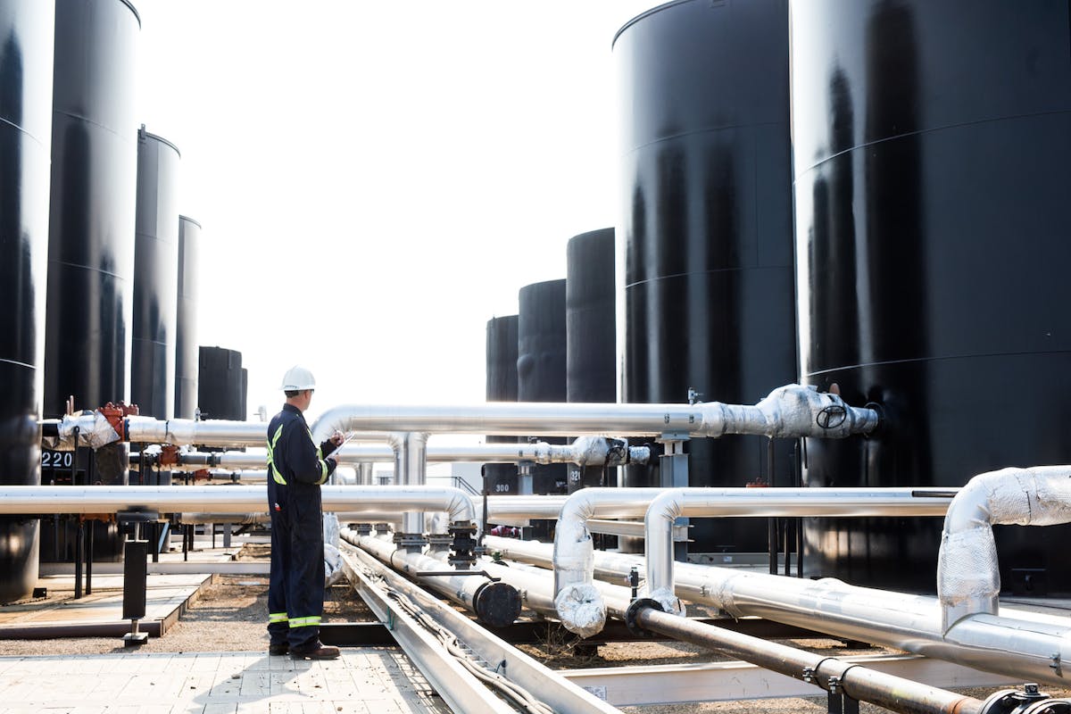 An oil worker monitoring large drums and pipes.