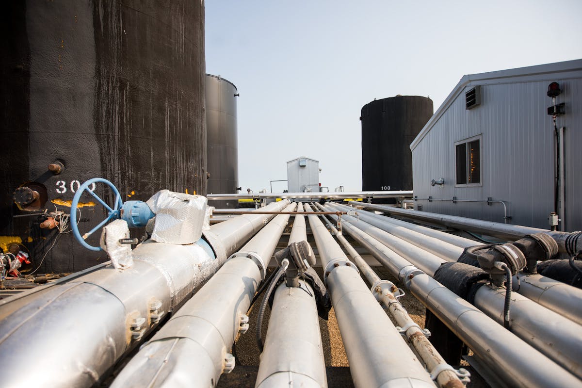 Oil rig pipes, between large barrels and a shed.
