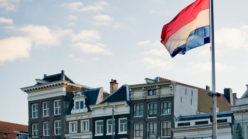 A Dutch flag waving above traditional buildings in the Netherlands.