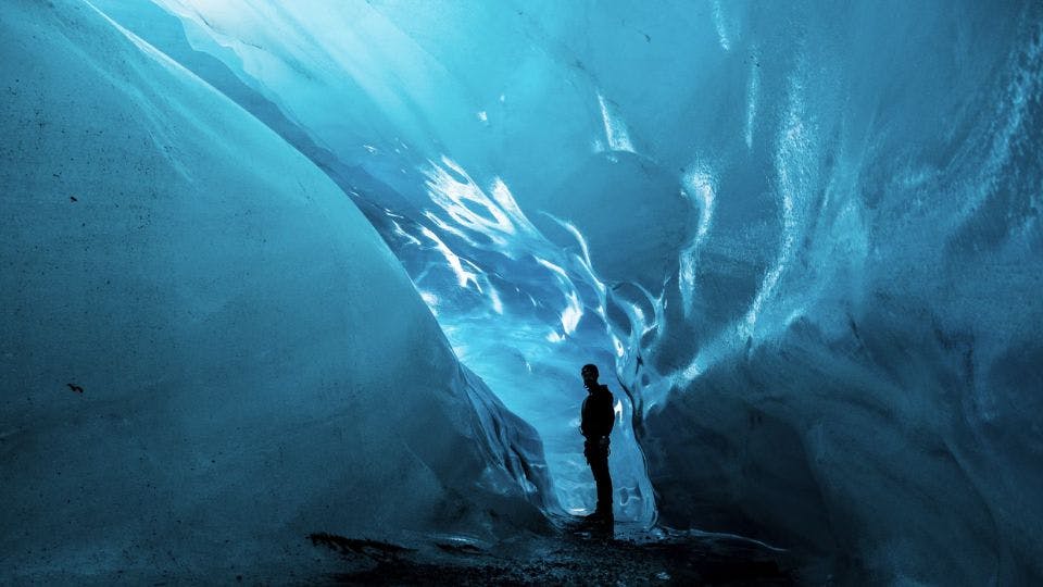 Man standing inside a blue ice cave.