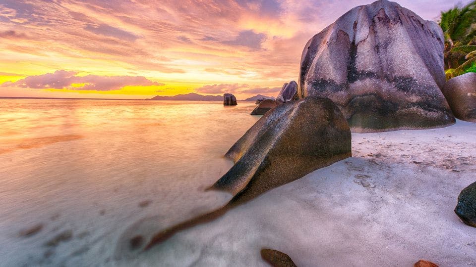 Sunset over beach with large rocks.