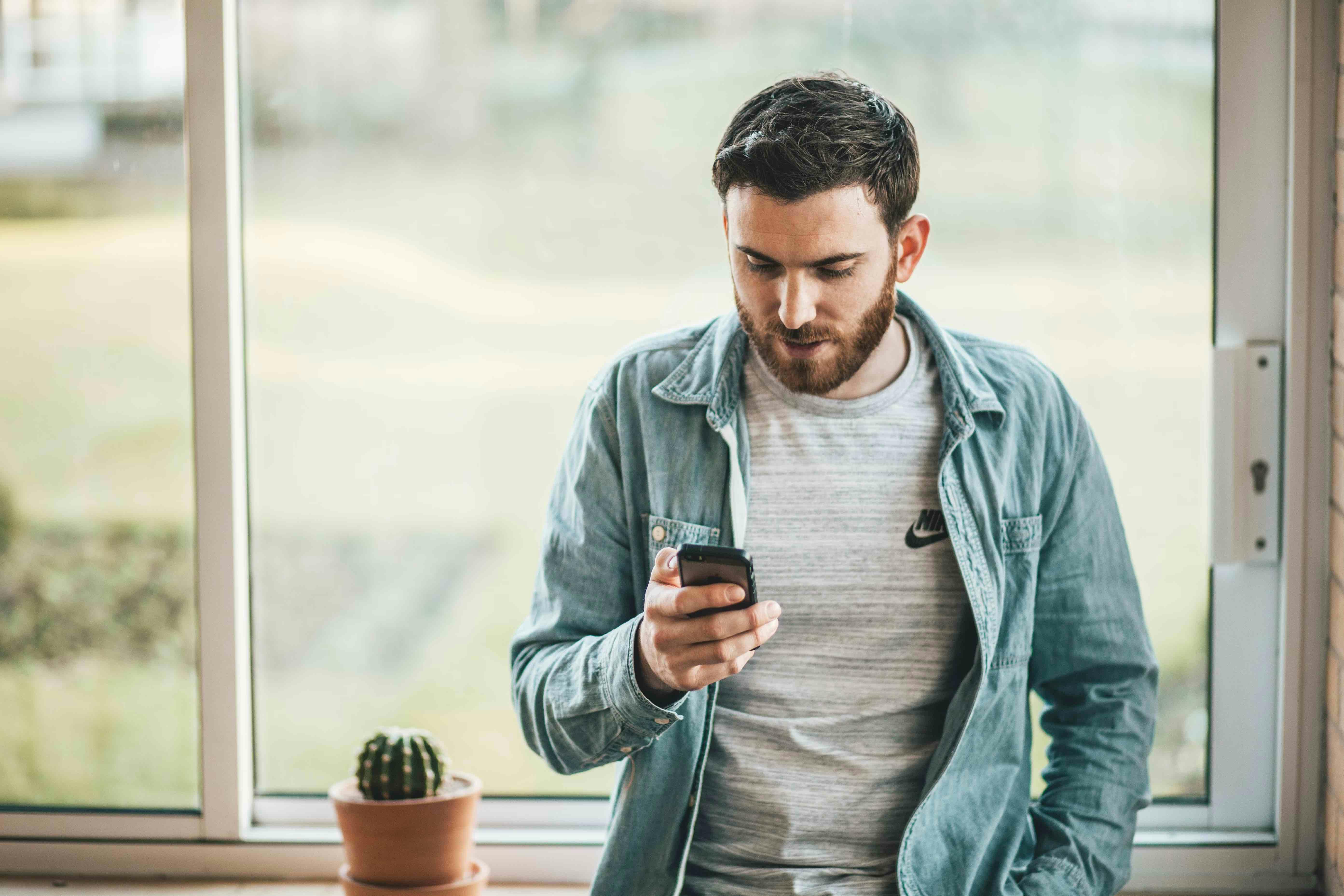 Een man met baard kijkt op zijn mobiel om online te bankieren.
