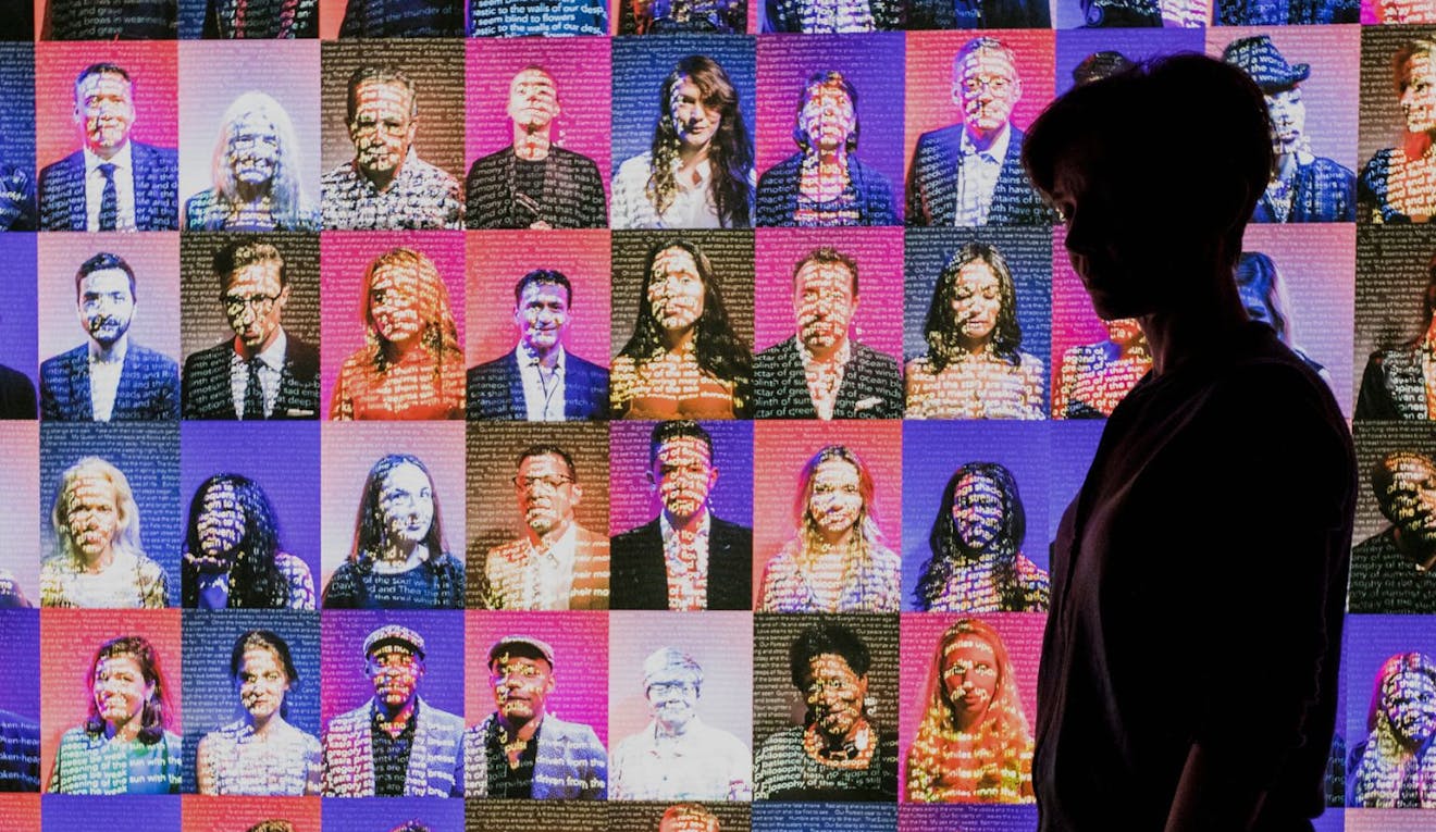 A person stands in front of a giant screen showing AI depictions of human portraits.
