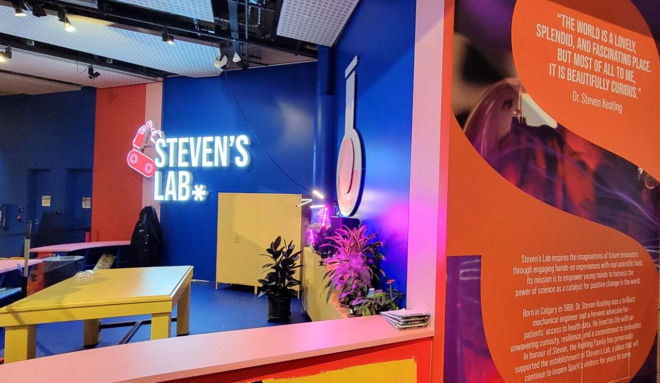 An open workshop called Steven's Lab that has bright blue and orange walls with a wrap around pink lab counter.