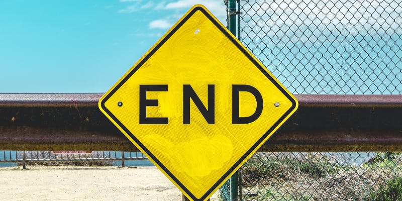 Bright yellow 'End' road sign against a blue sky