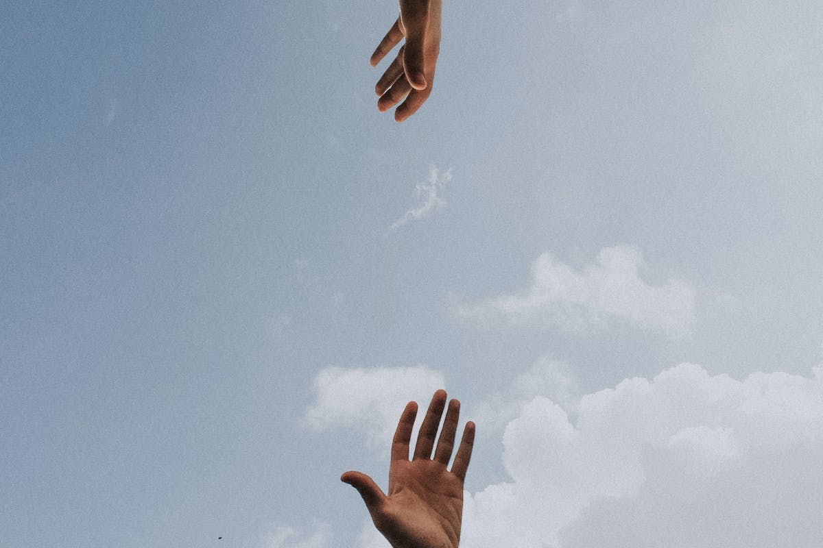 Two hands reaching towards each other in front of a blue sky.